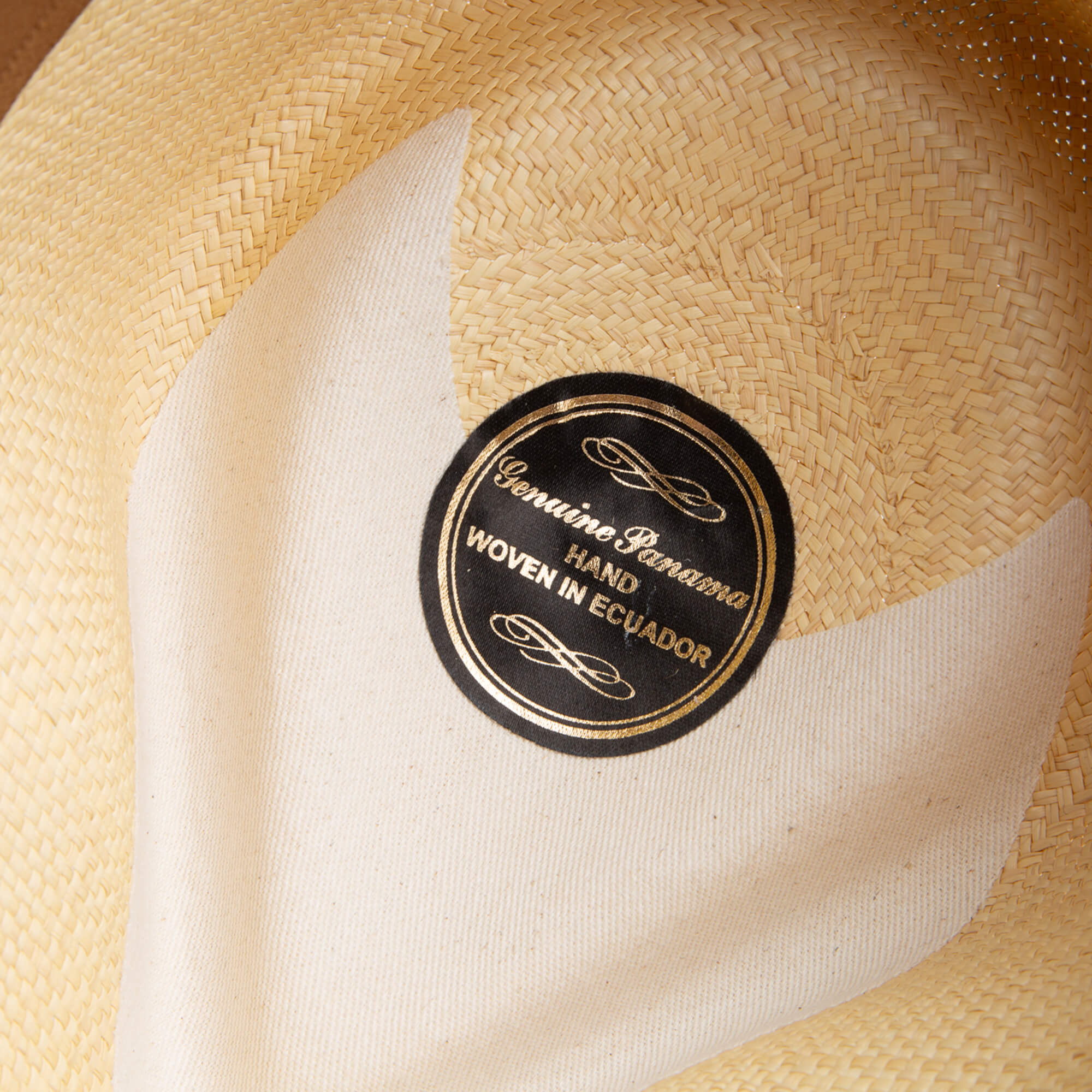 Close-up of the John Sr. teardrop fedora by Goorin Bros., handwoven in Ecuador from toquilla straw, featuring a black and gold "Genuine Panama" label and offering stylish sun protection with 50 UPF.
