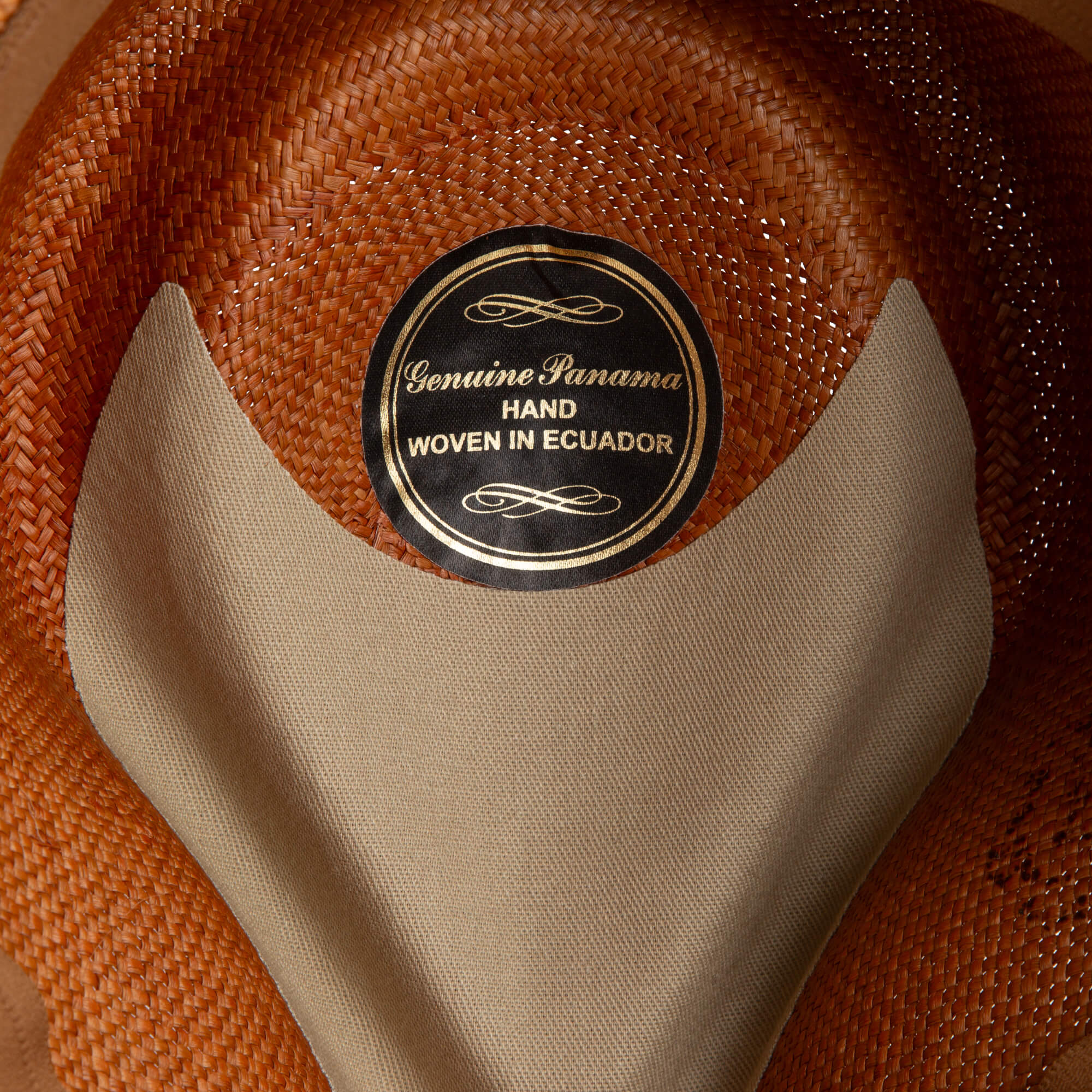 Close-up of the Goorin Bros. John Sr. fedora, a woven brown toquilla teardrop hat with "Genuine Panama, Hand Woven in Ecuador" label, partially covered by a beige fabric band for extra sun protection.