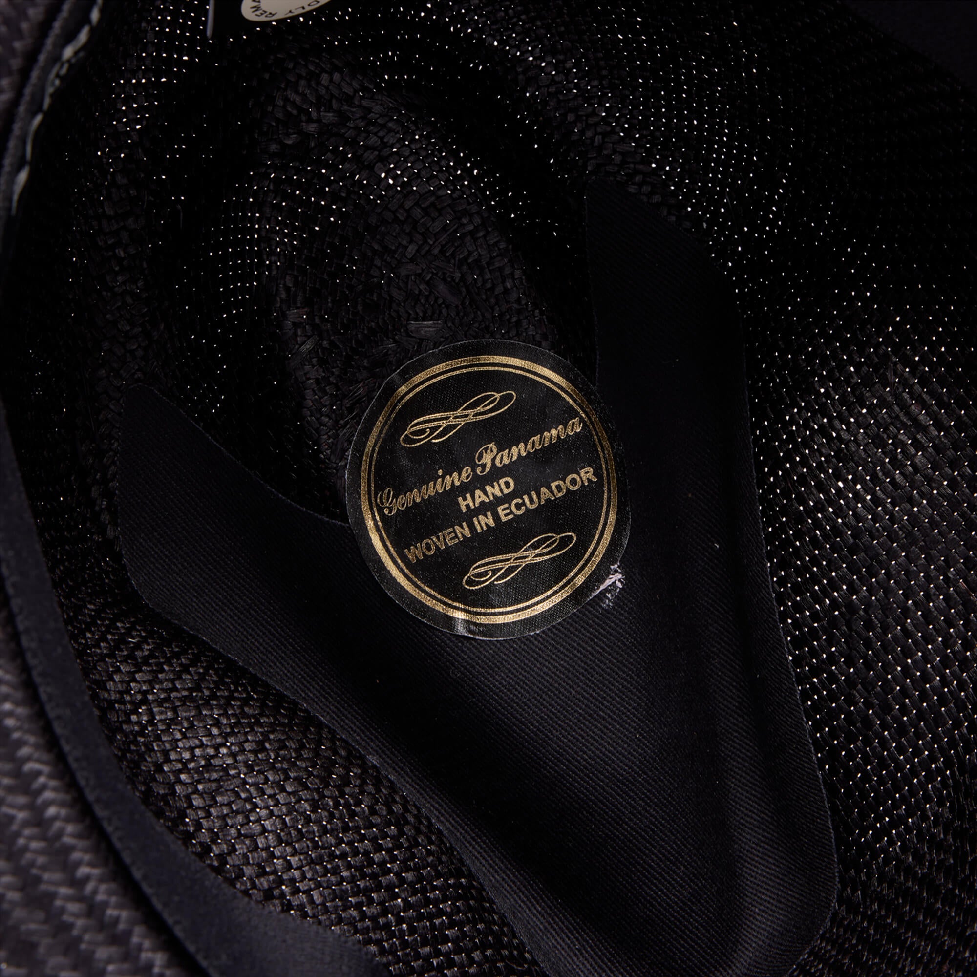Close-up of a Goorin Bros. Hartman hat’s interior label reading “Genuine Panama, Hand Woven in Ecuador” in gold and black, crafted from 100% toquilla straw and finished with a neat grosgrain hat band.