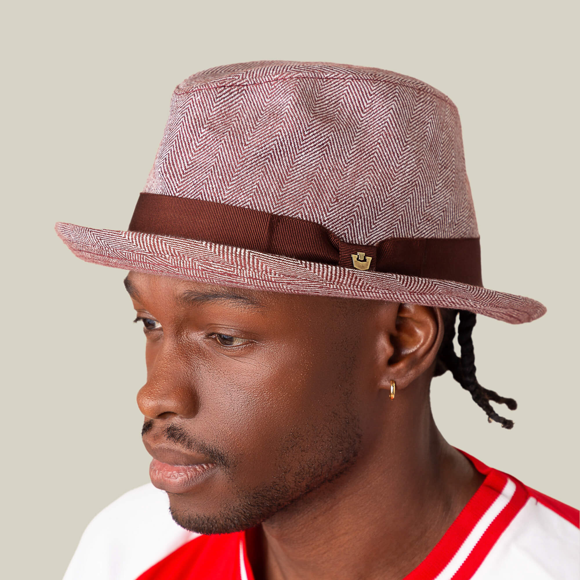A man wearing a red and white shirt and the Zig Zag Big Stepper fedora by Goorin Bros., featuring a brown band and subtle herringbone pattern, faces left against a plain background.