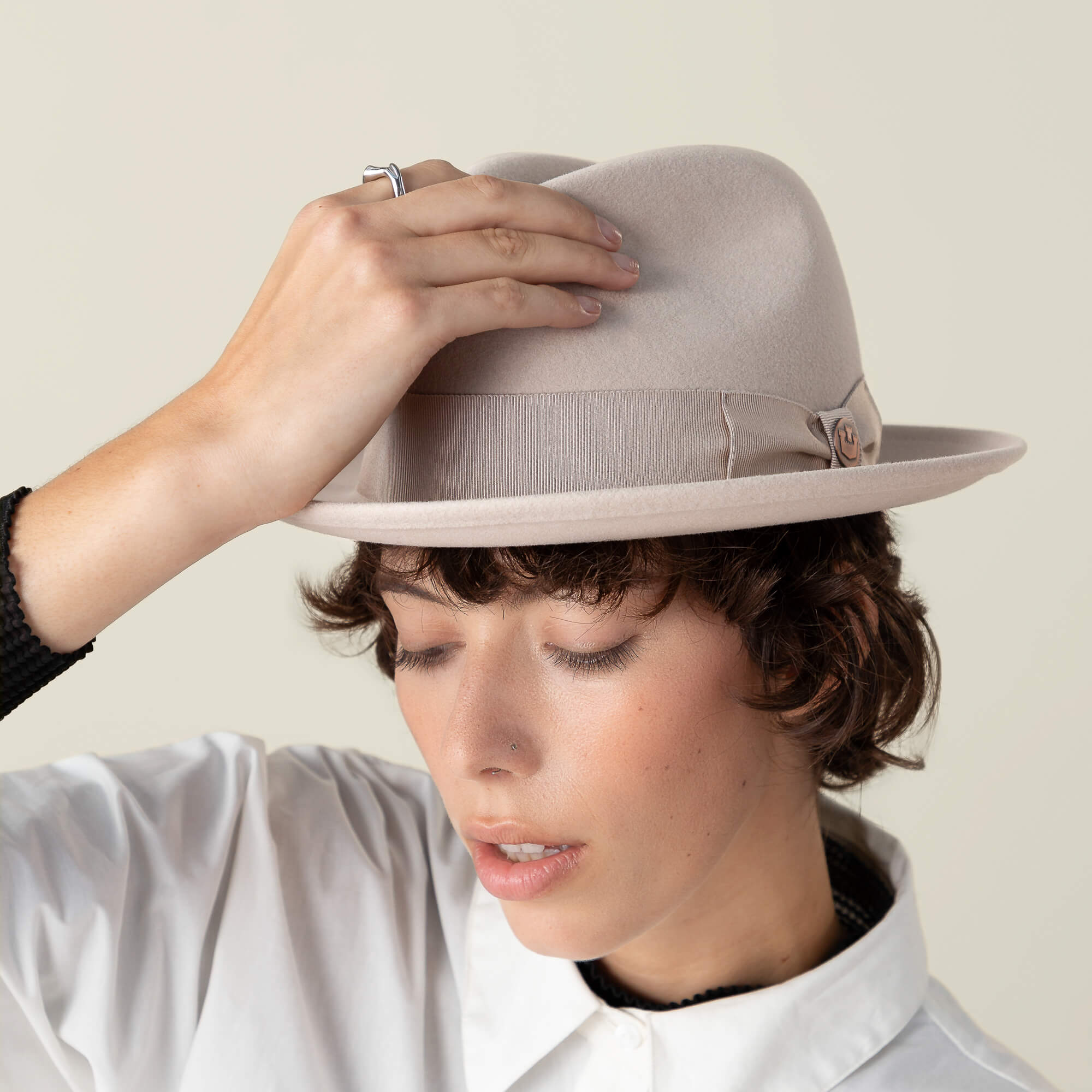 Person wearing the Goorin Bros. "Dean the Butcher" fedora and a white collared shirt, tilting the hat with one hand, eyes closed, against a plain background.