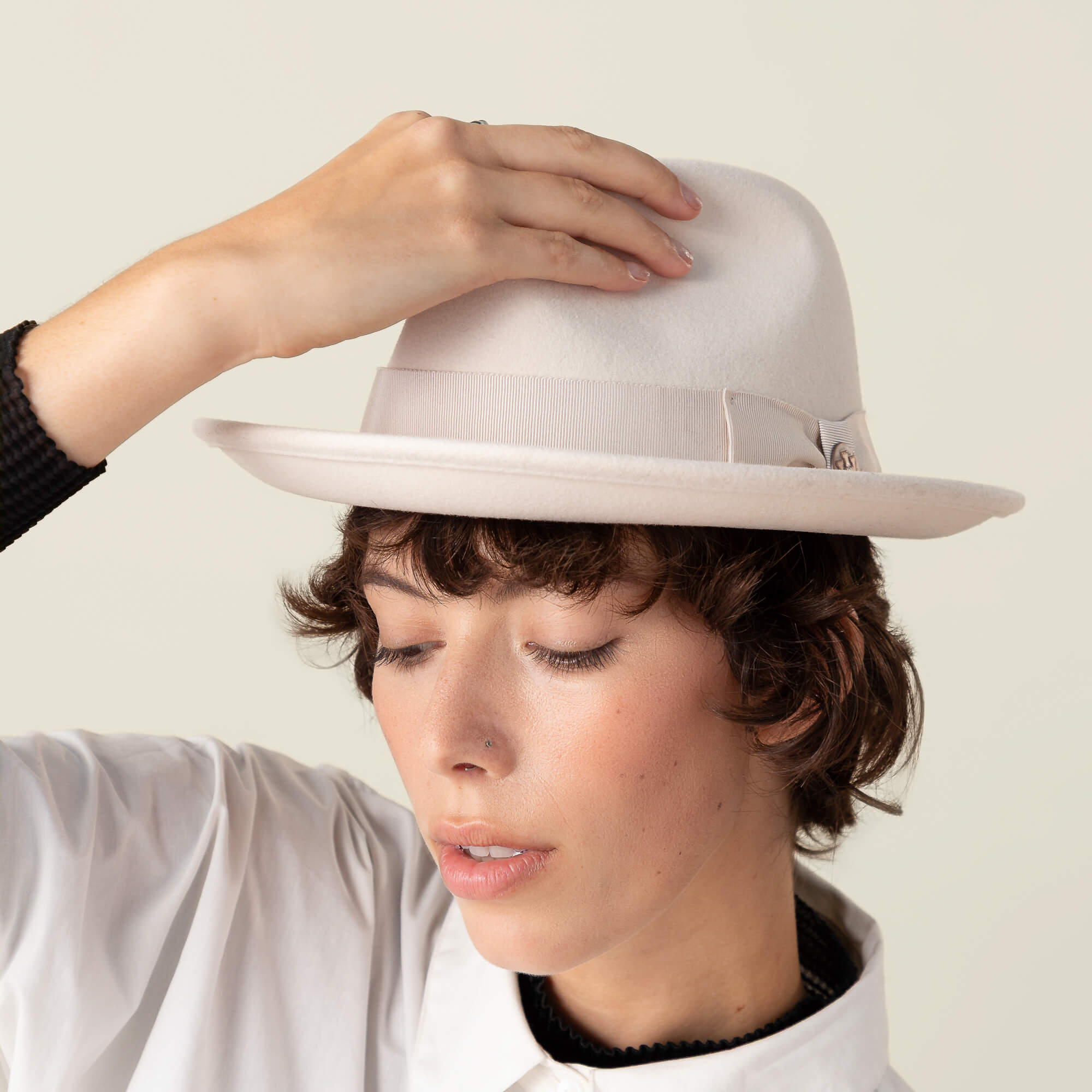 A person wearing the Goorin Bros. "Dean the Butcher" fedora with a grosgrain hatband and white shirt, tilting their head down and touching the brim.