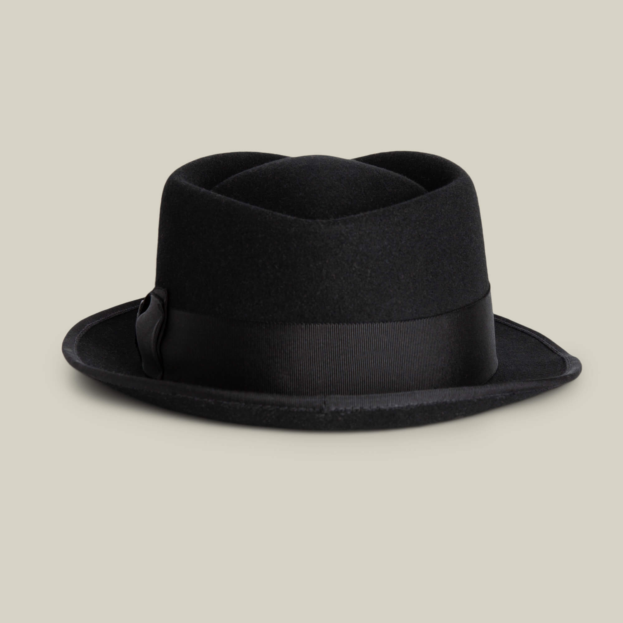 The Goorin Bros. Slick Carter is a black wool short brim pork pie hat with a wide grosgrain ribbon band, shown against a plain beige background, embodying effortless style.