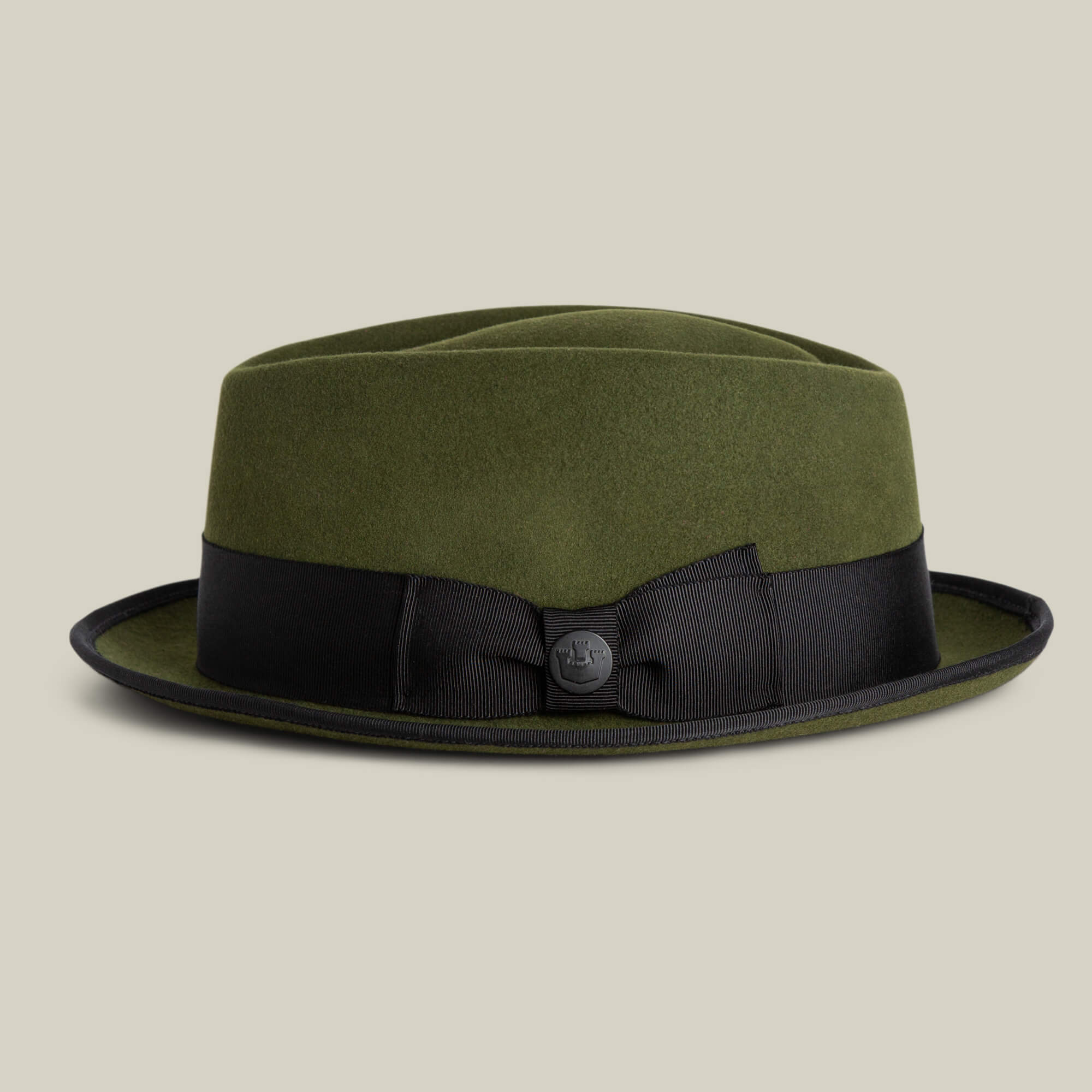 The Goorin Bros. Slick Carter is an olive green wool short brim fedora with a black ribbon band and small decorative button, shown against a plain beige background, reflecting effortless style.
