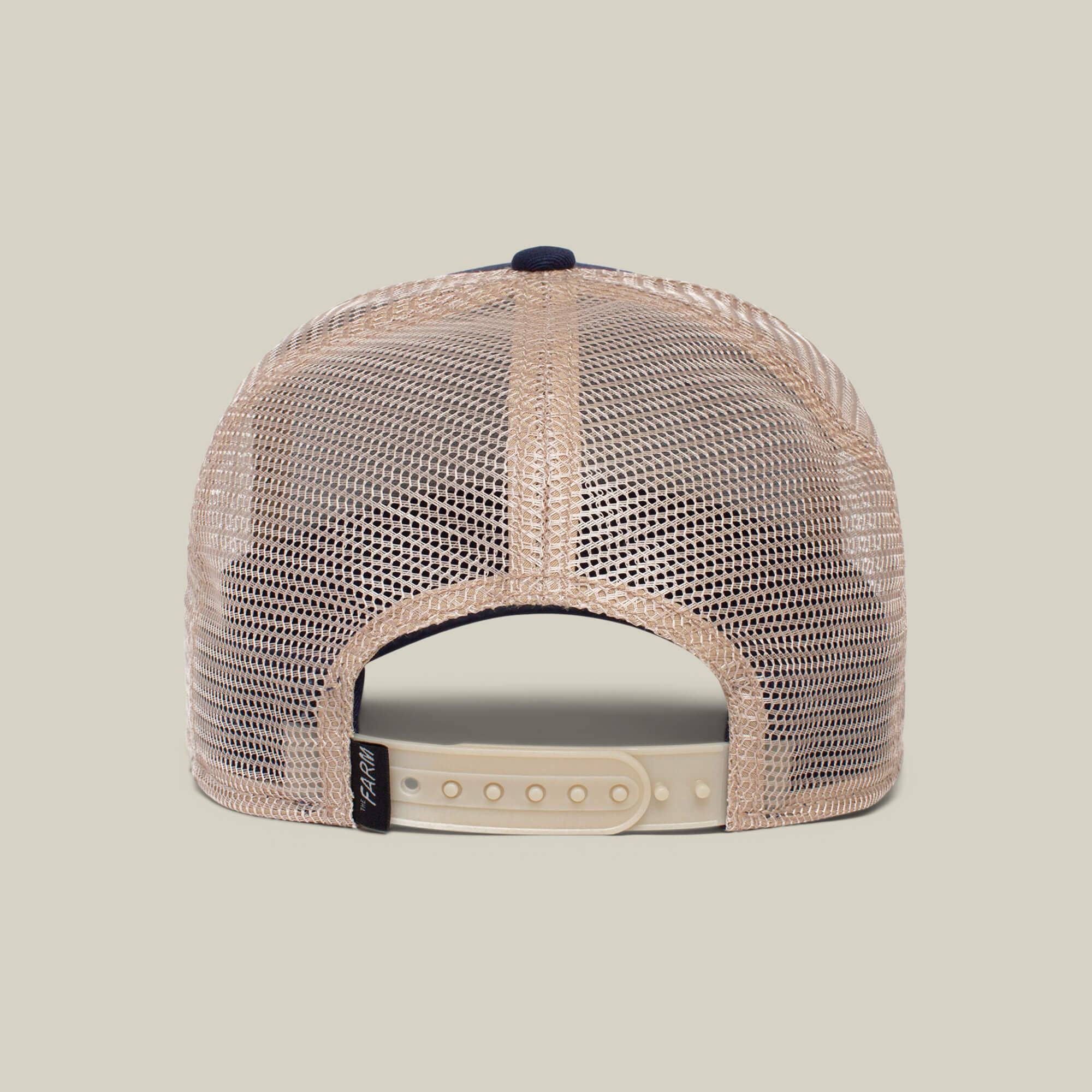 The back view of The Cock by The Farm—a beige mesh trucker hat with white adjustable snapback and black left-side tag—subtly features a rooster, the timeless symbol of resurrection.