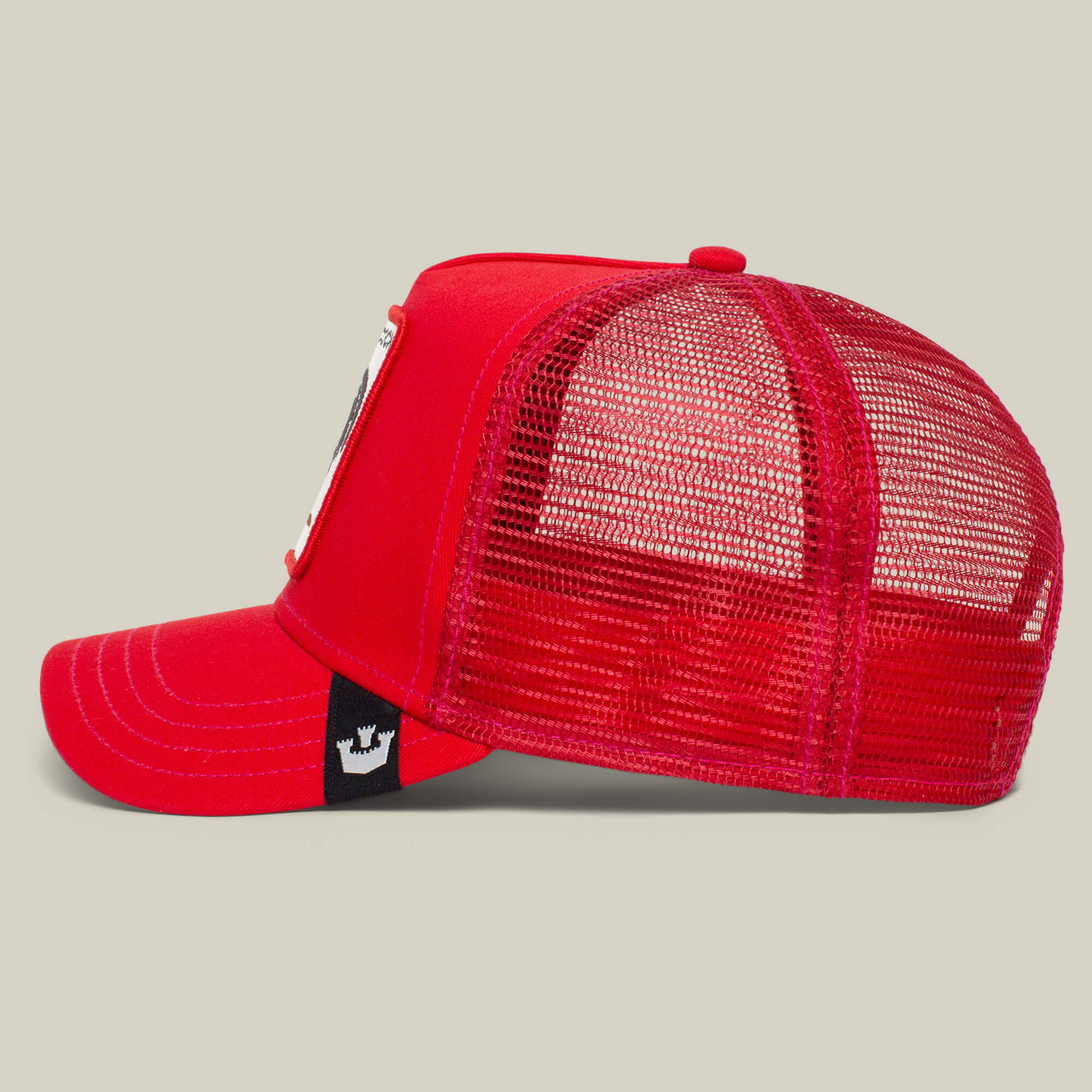 The Farm’s “The Cock” is a red mesh trucker hat with a curved brim, front patch, and black side tag, shown in profile. It features a rooster motif—symbol of sexuality and resurrection—against a plain background.