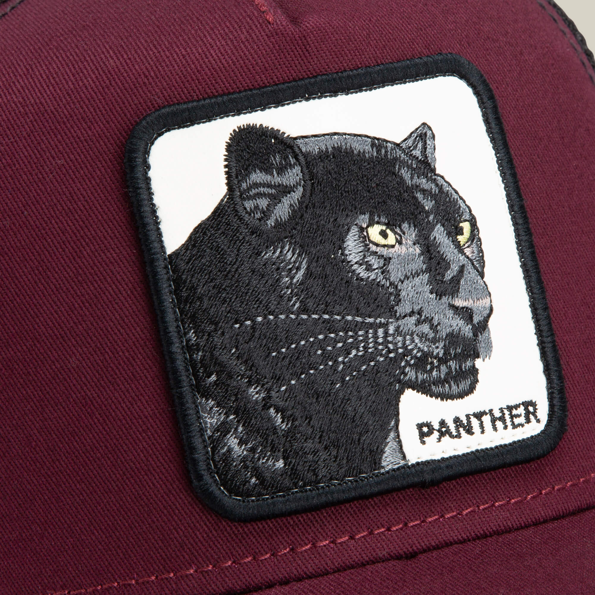 Close-up of The Panther trucker hat by Goorin Bros., showcasing a maroon design with a rectangular patch featuring an embroidered black panther and the word "PANTHER" in capital letters.