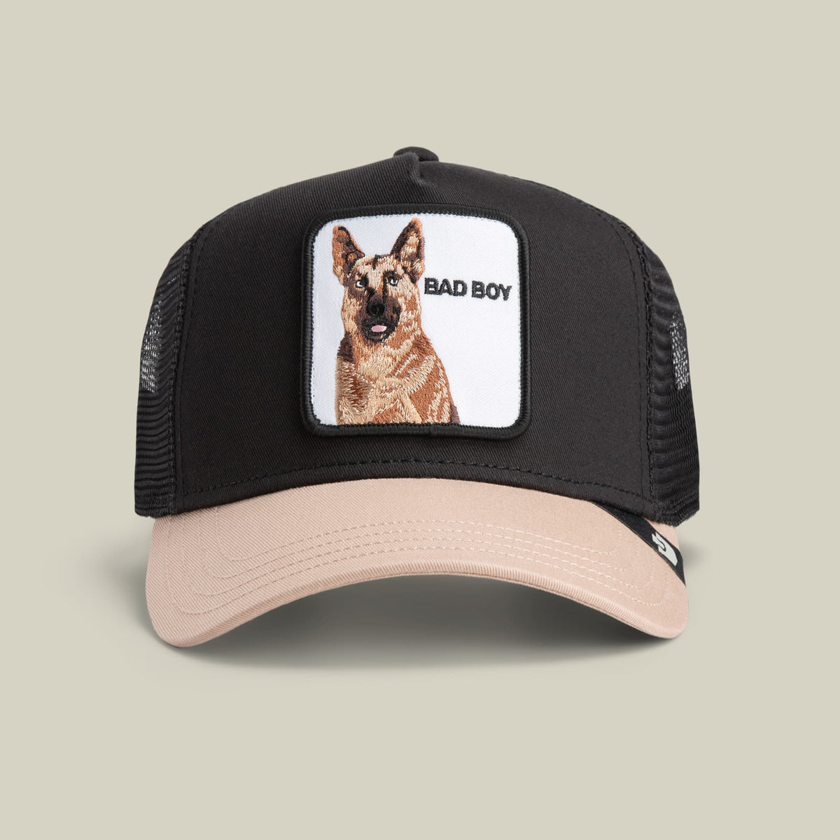 The Bad Boy by Goorin Bros is a black and beige trucker hat featuring a mesh back and a embroidered German Shepherd patch with "Bad Boy" text on the front panel.