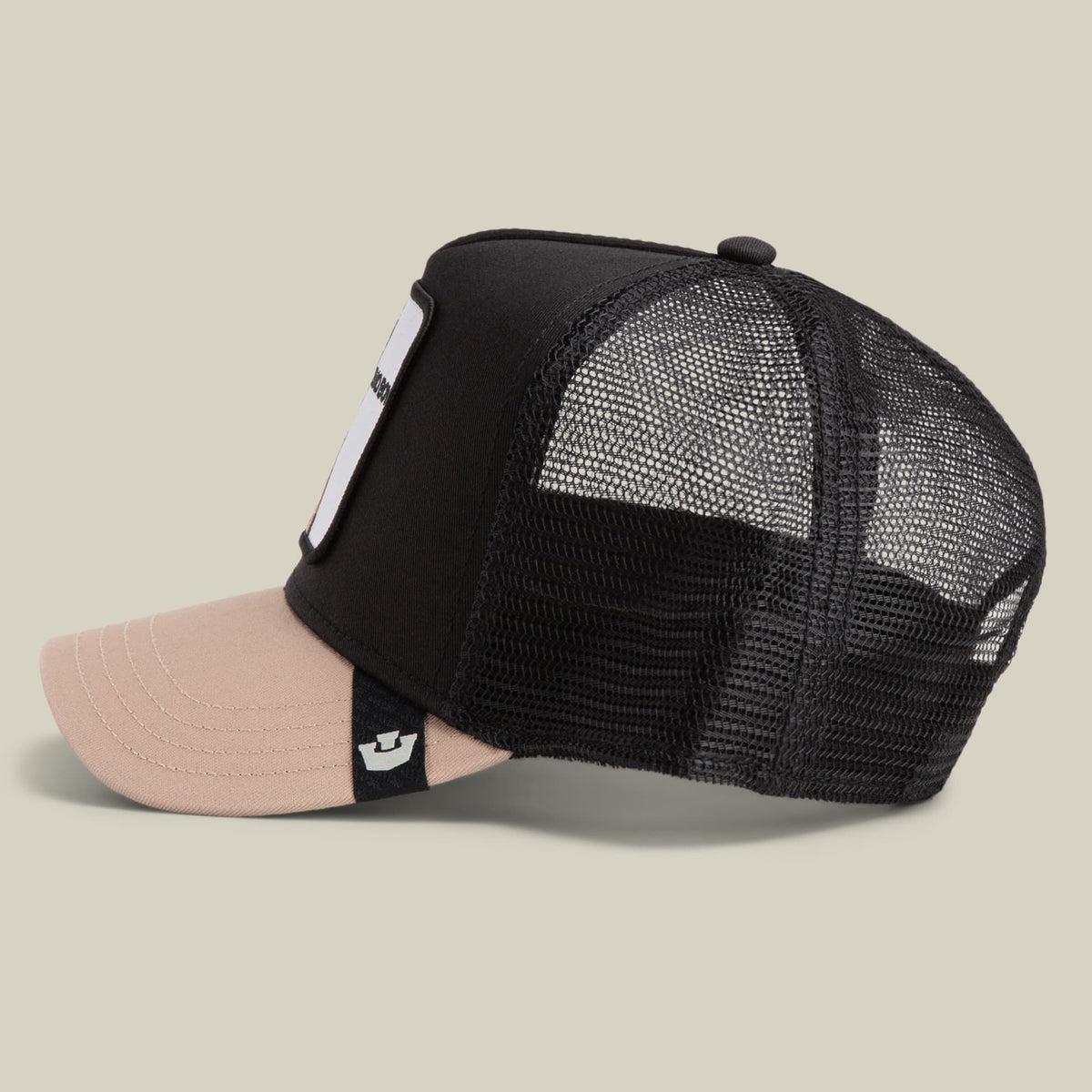 The Bad Boy by Goorin Bros is a black and beige mesh trucker hat with a two-tone design, featuring a black mesh back and black fabric front panel with a light pink brim, displayed on a neutral studio background.