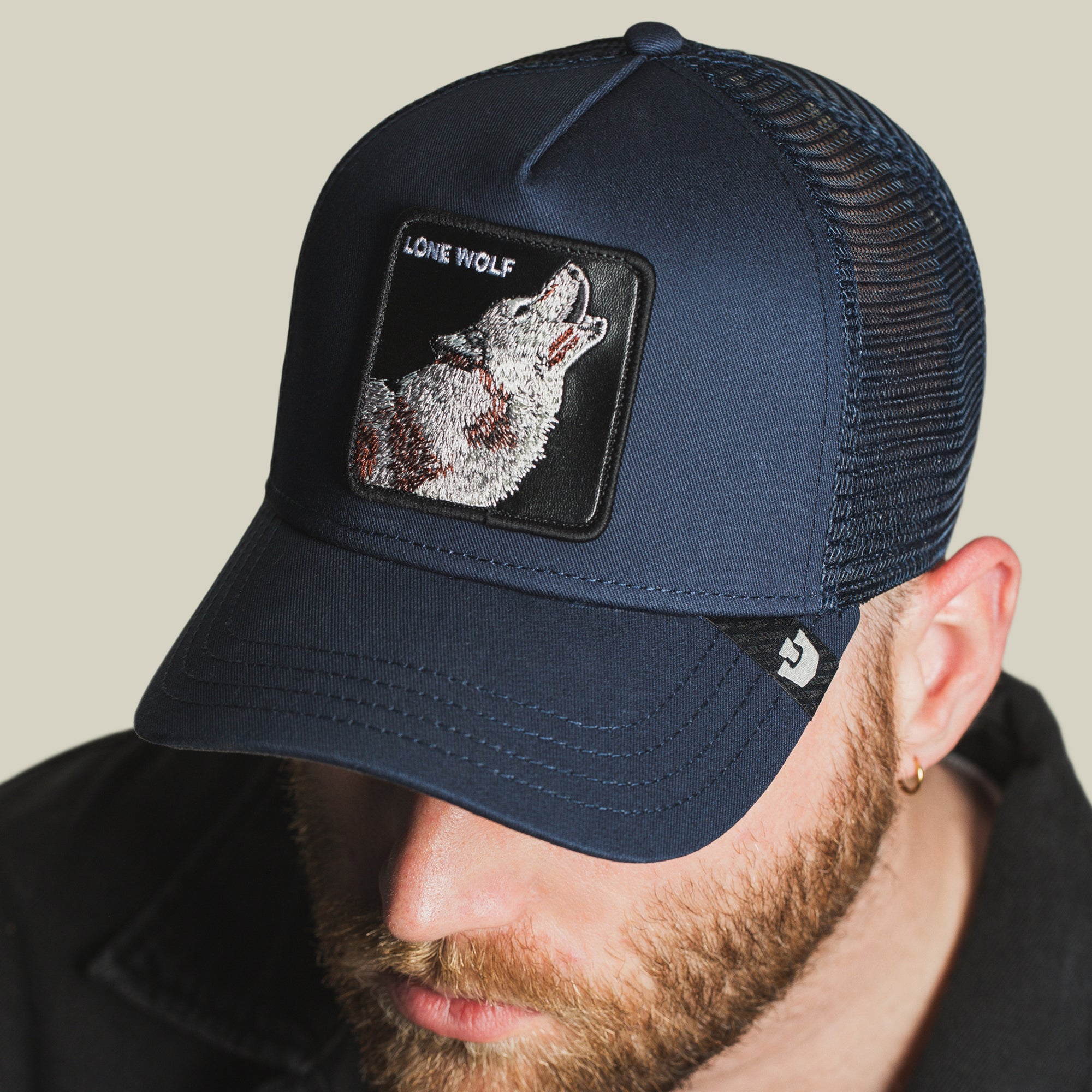 A man sports The Lone Wolf mesh trucker hat by The Farm, featuring a howling wolf patch and "LONE WOLF" text—a bold accessory for the independent spirit.