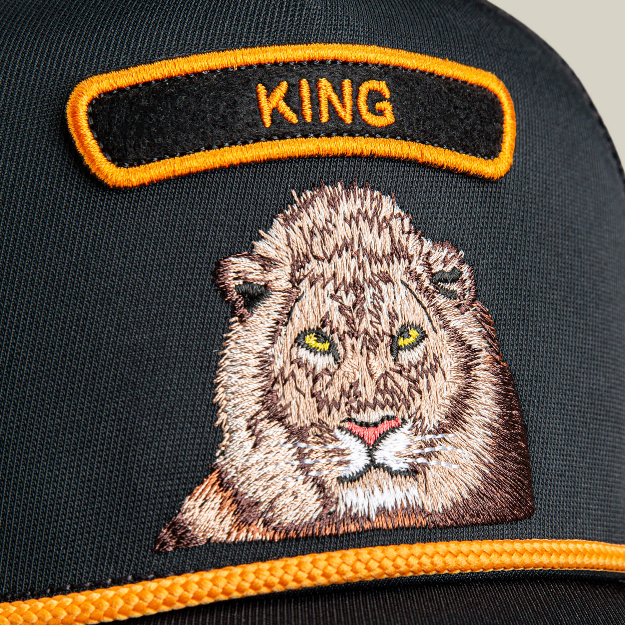 Close-up of The Farm’s GB2 Lion black cap with an embroidered lion face and “KING” in yellow, symbolizing strength and authority.