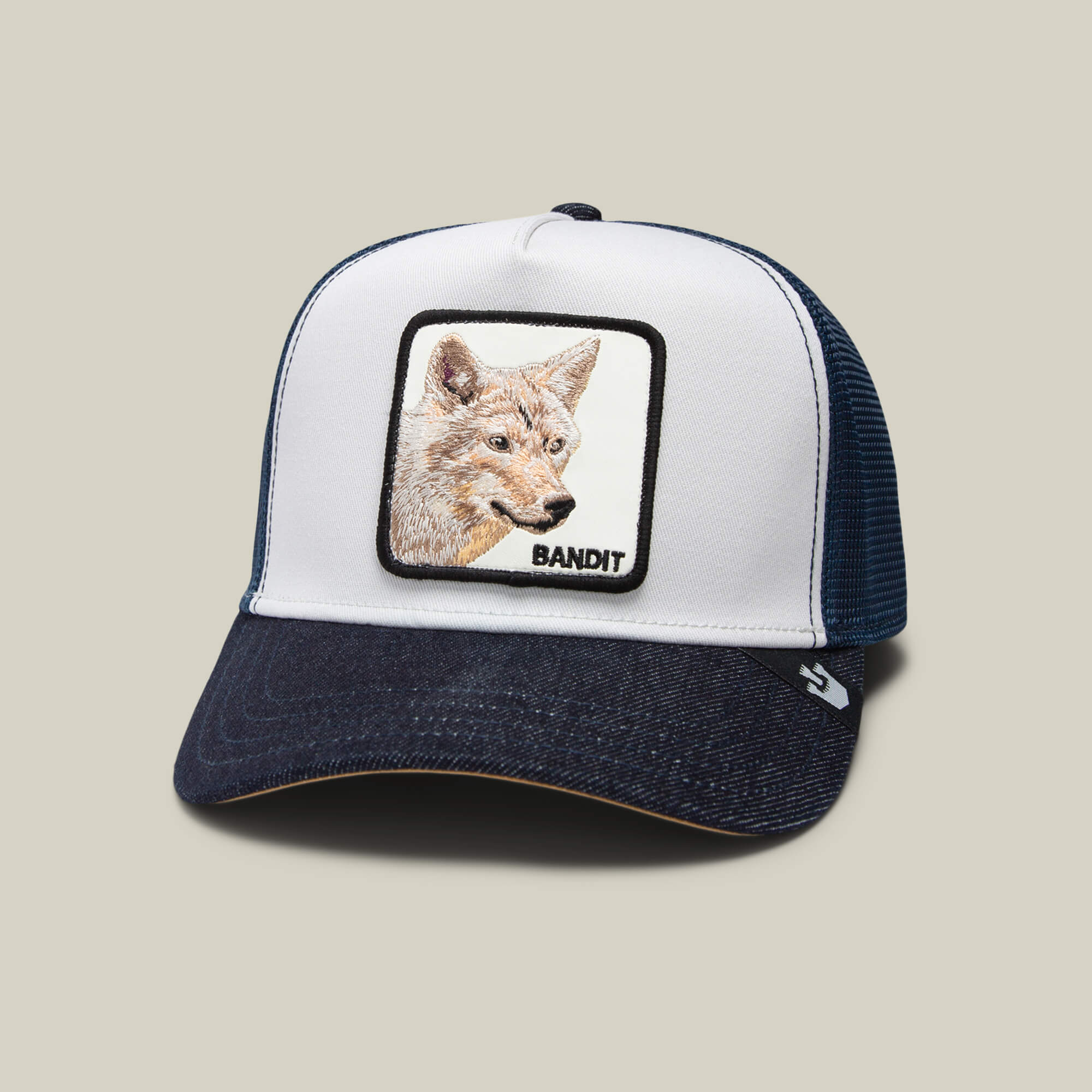 The Bandit Coyote by The Farm is a white and navy trucker hat with an embroidered coyote head and "BANDIT" patch on the front—ideal for showcasing your wild spirit.