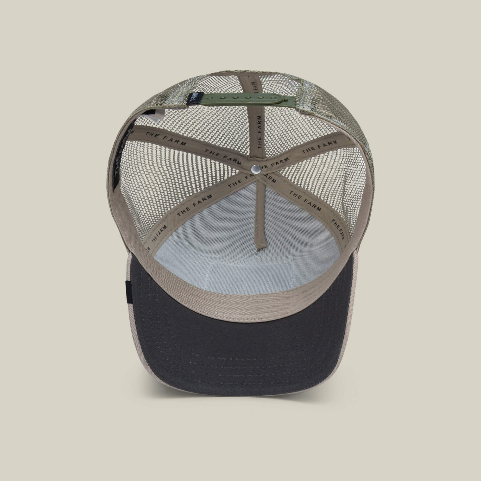 An inside view of The Farm's The Bandit Coyote beige and black trucker hat reveals mesh back panels, an adjustable strap, and THE FARM on the inner sweatband—crafted for those with outlaw energy.