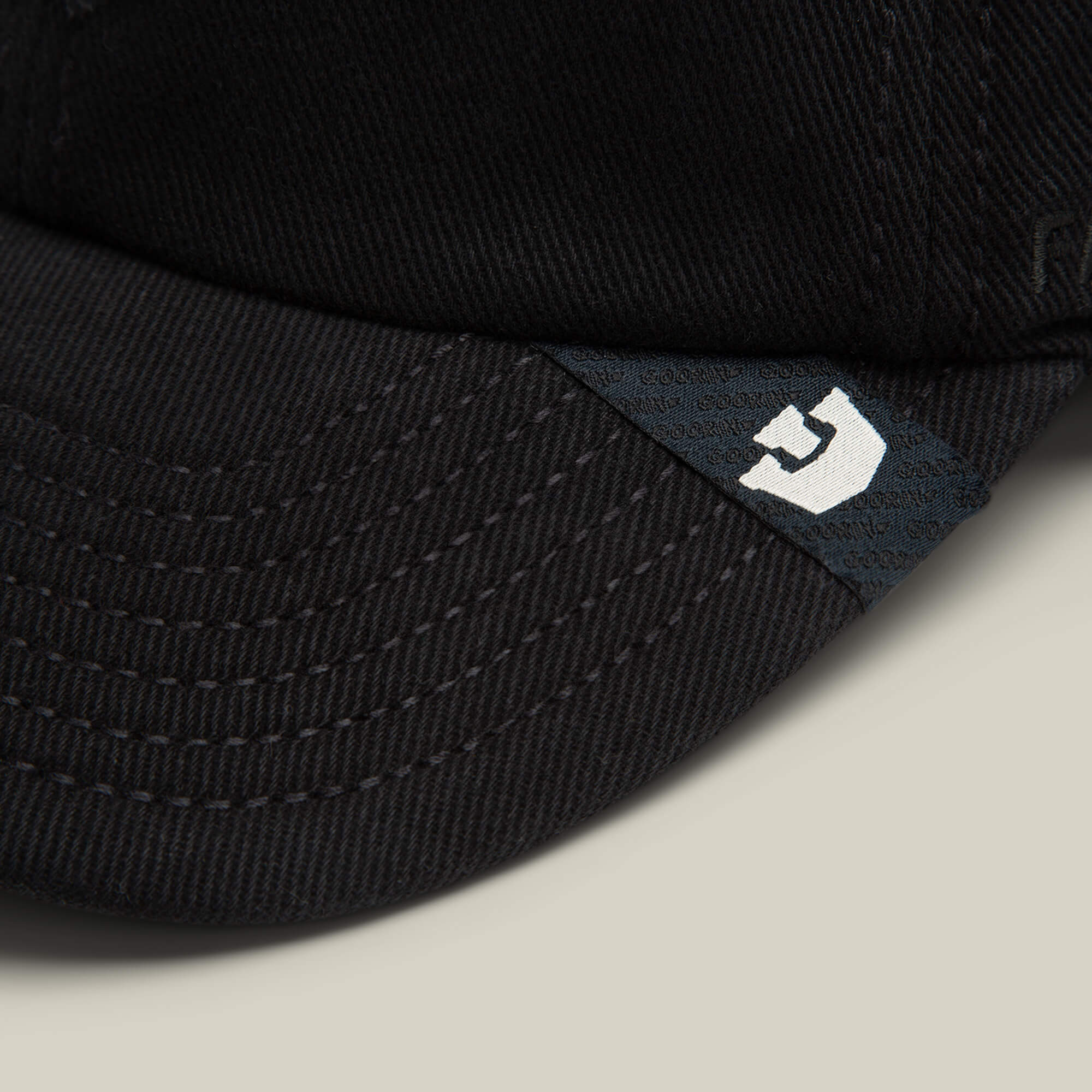 Close-up of the brim on Goorin Bros. Fine Headwear papa cap, featuring visible stitching and a small black tag with a white stylized letter G, showcasing premium quality.