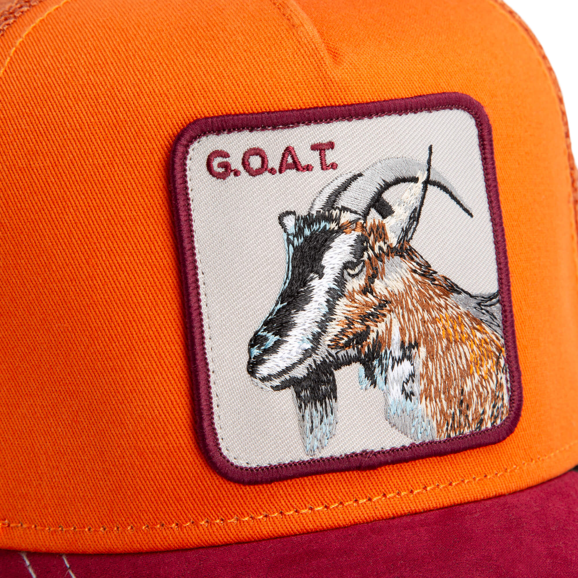 Close-up of an orange and red The Farm "Greatest Grazer" cap with a stitched patch showing a goat illustration and the text G.O.A.T. All Sales Are Final.