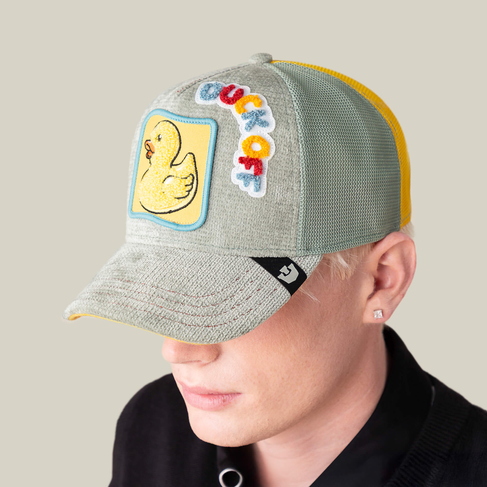 A person wears a Goorin Bros. Ducking Autocorrect hat featuring a yellow duck patch and colorful "duckoff" text, pairing it with short blond hair and a black shirt for a playful vibe.