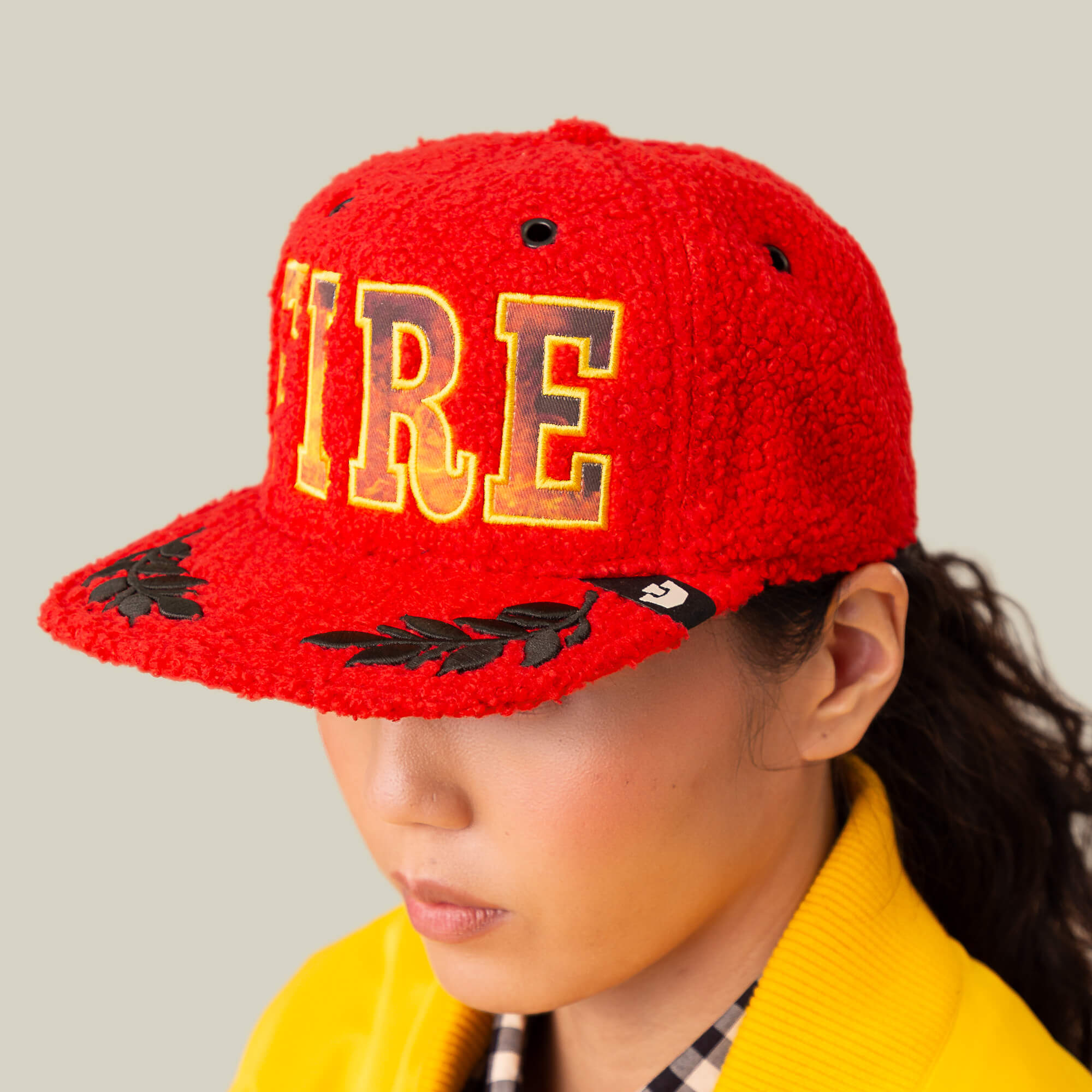 Someone wears the Goorin Bros. Hot Fire sherpa hat with bold yellow "FIRE" letters and black laurel designs, paired with a yellow collared jacket, set against a plain background.