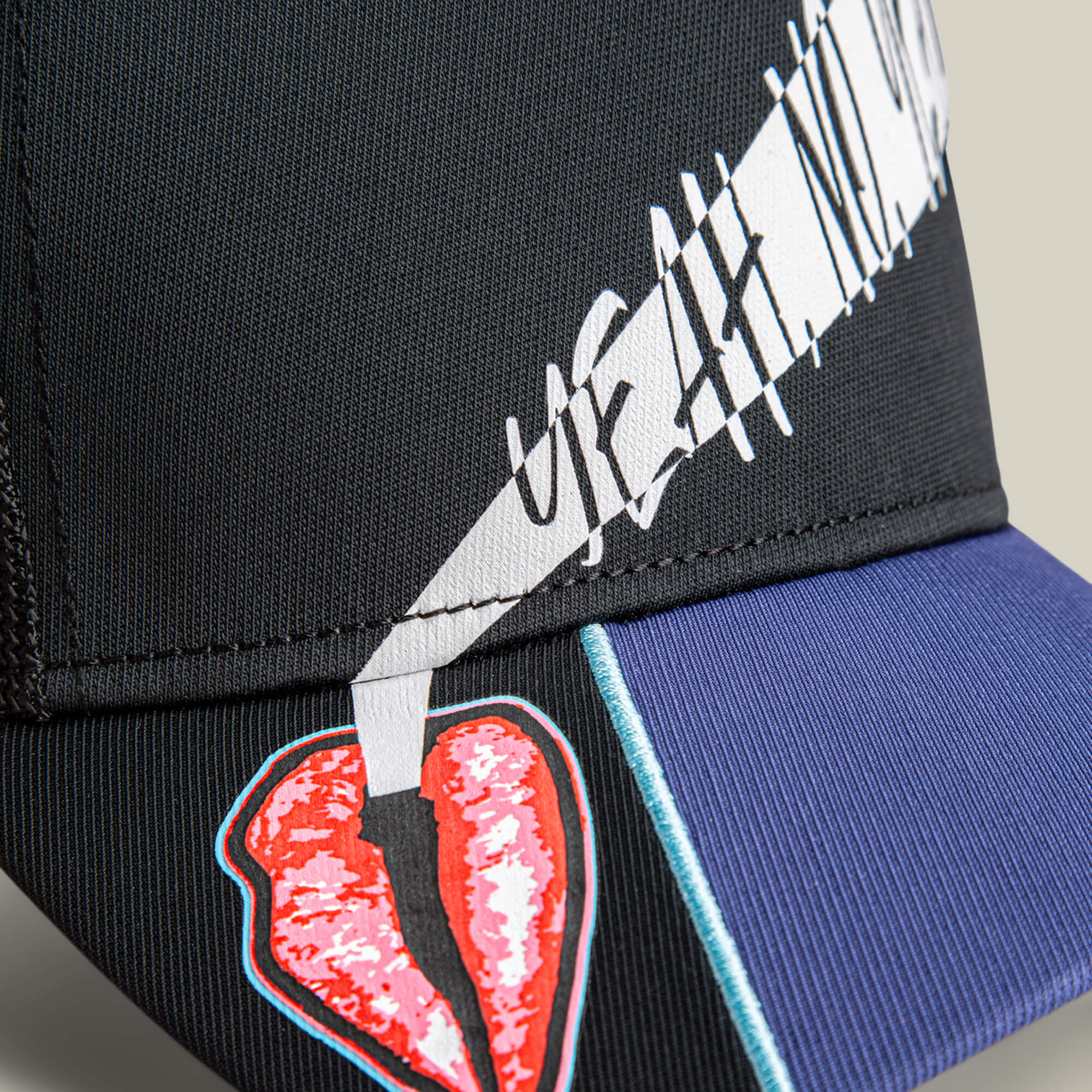 Close-up of the Goorin Bros. "Means Yes" black and blue statement hat, featuring a red broken heart graphic and white stylized text, "yeah, nah," above the brim—a unique accessory for bold expression.