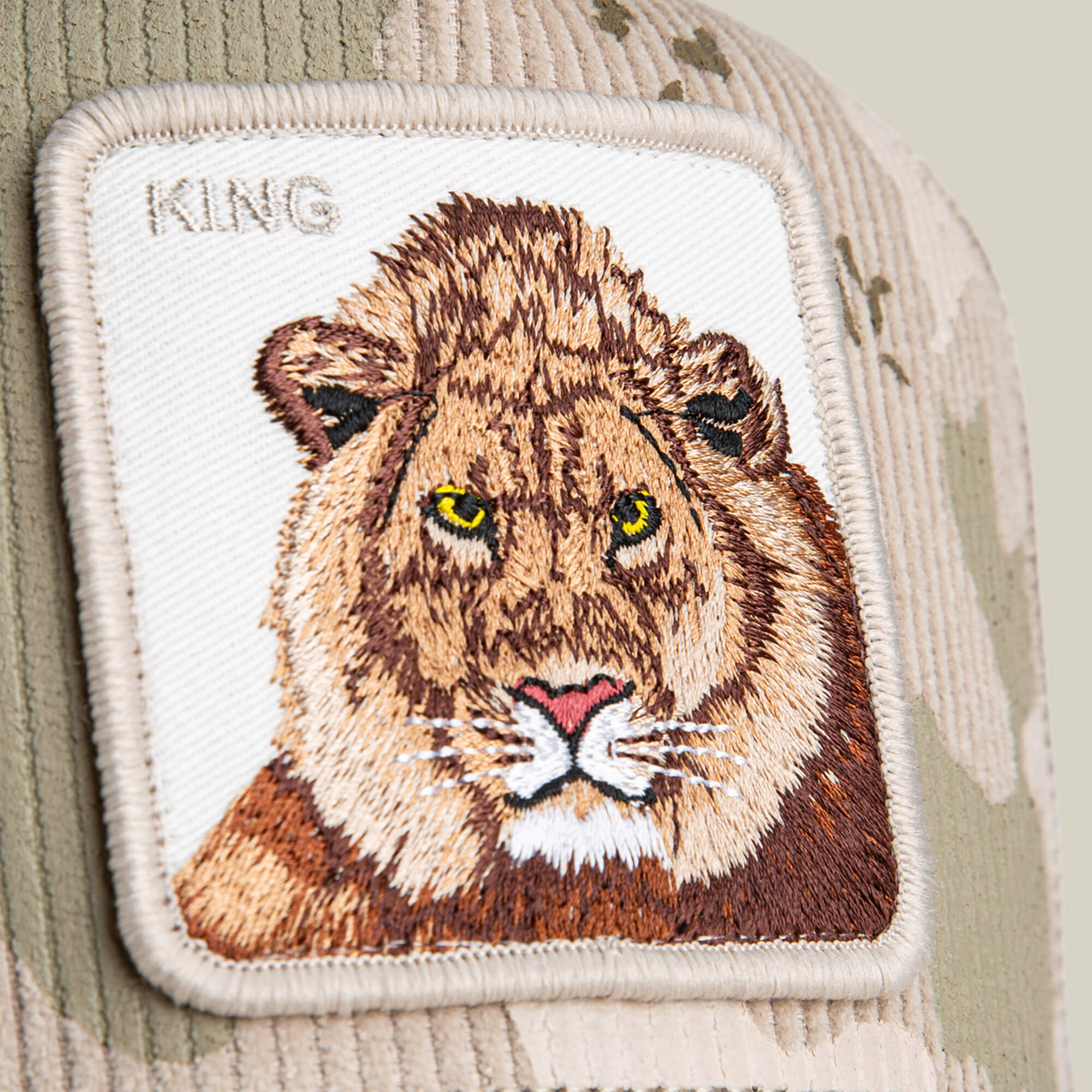 The Goorin Bros. King Camo hat is a khaki and beige corduroy cap with a rectangular patch featuring a lion’s face and “KING” stitched in the corner, blending classic style with subtle King Camo flair.