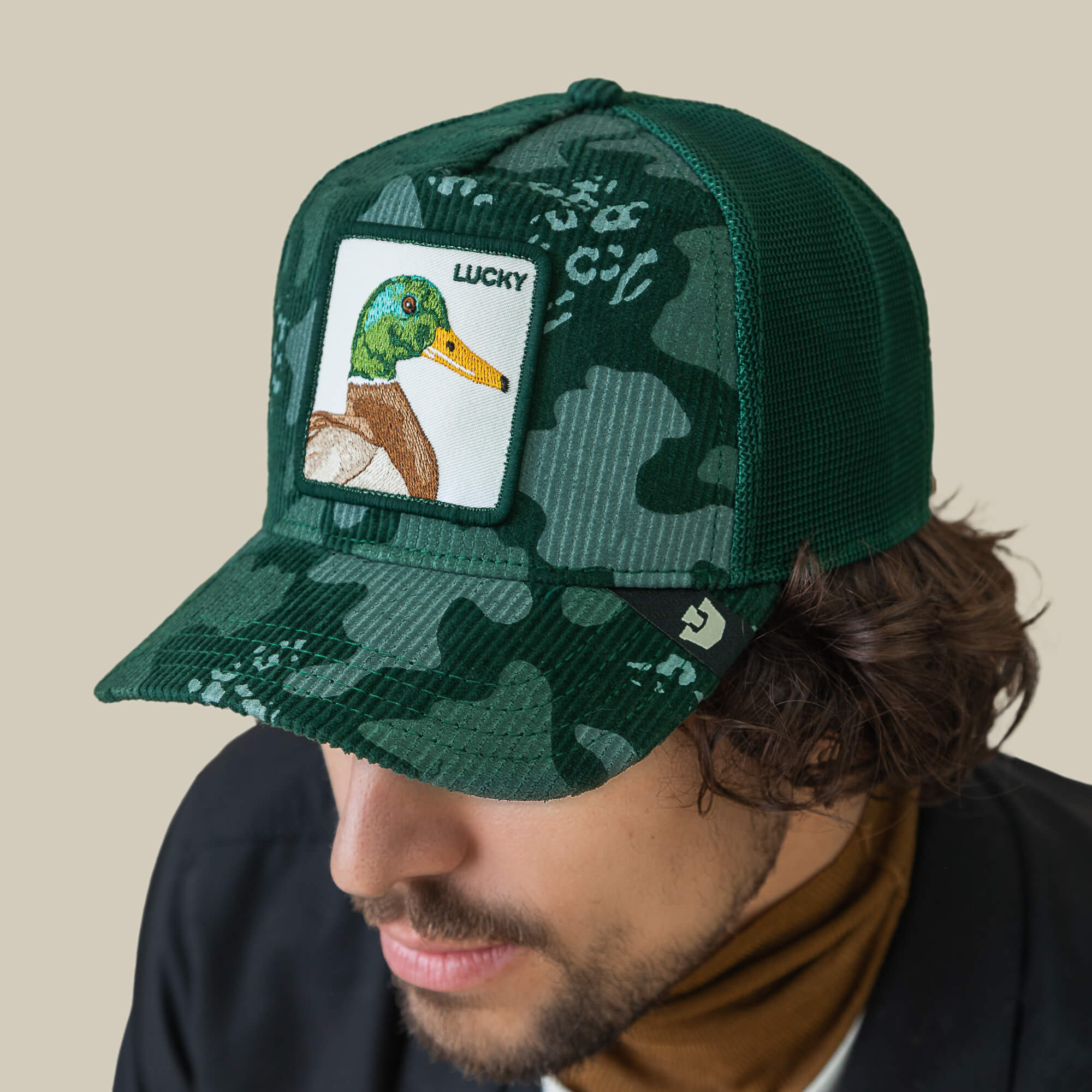 Man wearing the Duck Camo corduroy mesh cap by Goorin Bros., featuring a camo patch with a mallard duck and "LUCKY" embroidered above it.