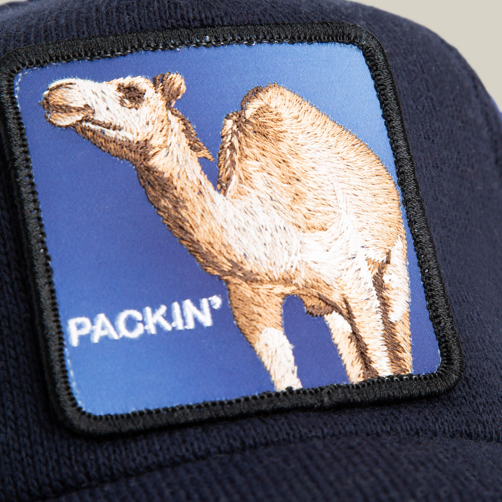 The "Don't Say Fudge" cap by Goorin Bros. is crafted from epic sweater material in navy blue, featuring a patch with a camel and the word PACKIN’ on a blue background for ultimate comfort.