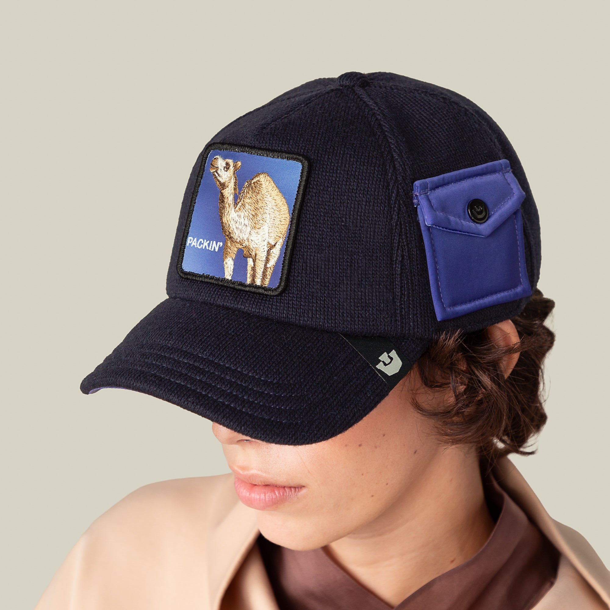 A person wears the Goorin Bros. "Don't Say Fudge" navy baseball cap, featuring a camel patch and small blue side pocket, made from epic sweater material, set against a plain light background.