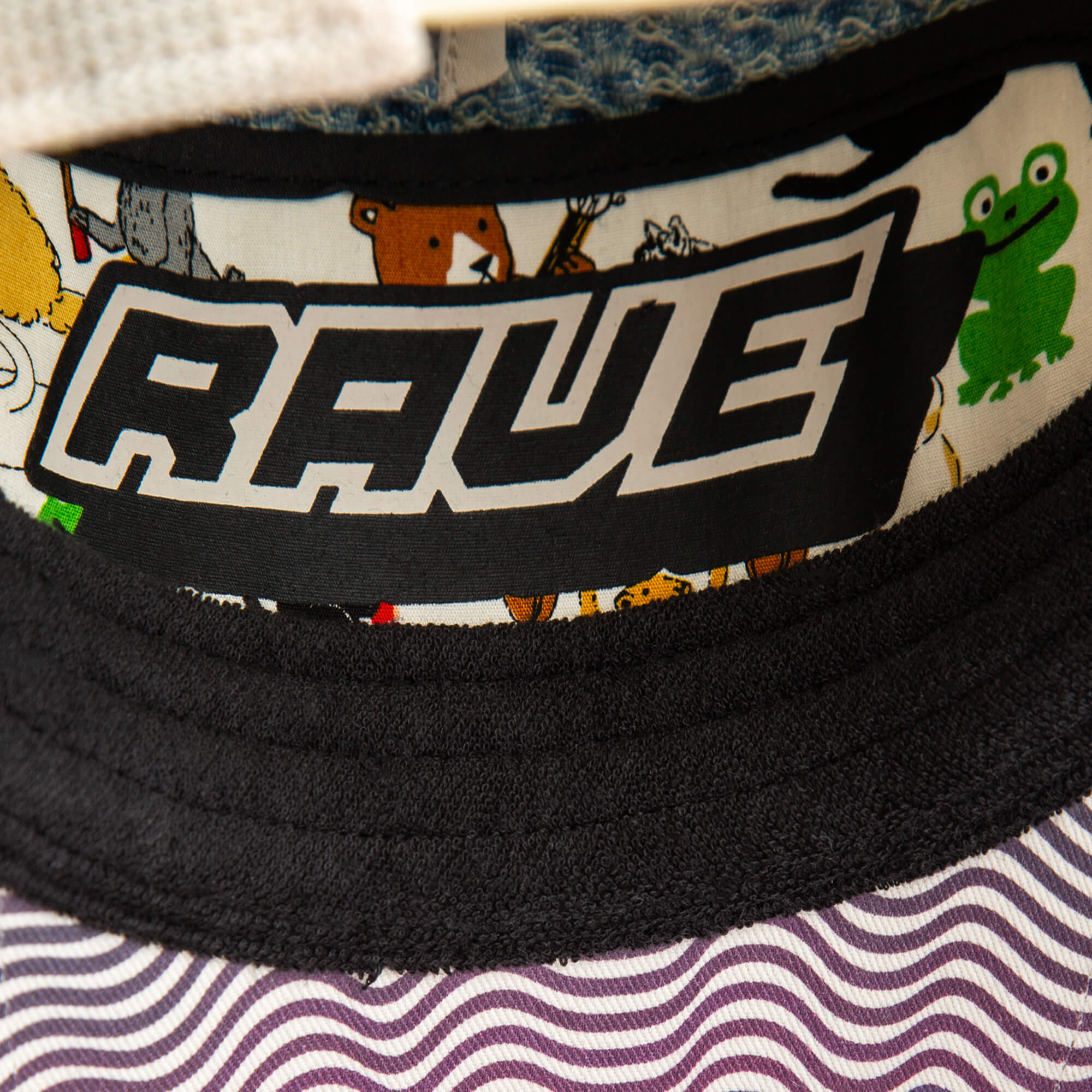A close-up of the Goorin Bros. Acid House hat, featuring a patterned brim and RAVE label inside, surrounded by cartoon animals like a green frog and brown bear, captures playful Acid House vibes perfect for any laser dome party.