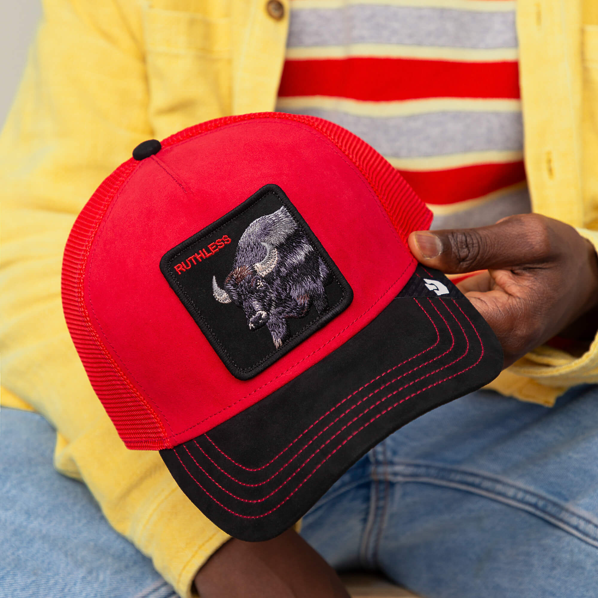 A person holds the “Suede Buffalo” trucker hat by Goorin Bros., featuring a black suede brim and a buffalo patch with “RUTHLESS” embroidered on the front in red and black.