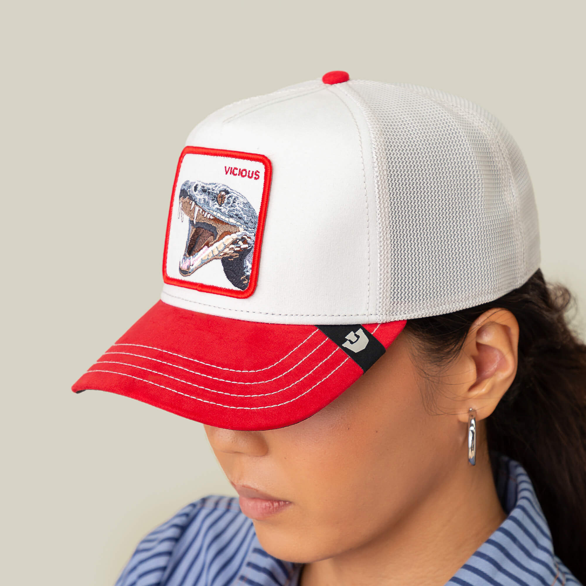 Sporting the Goorin Bros. Suede Snake trucker cap in white and red with a snake patch labeled "VICIOUS," this person radiates predator energy. Smooth suede adds comfort, while hoop earrings complete the look.