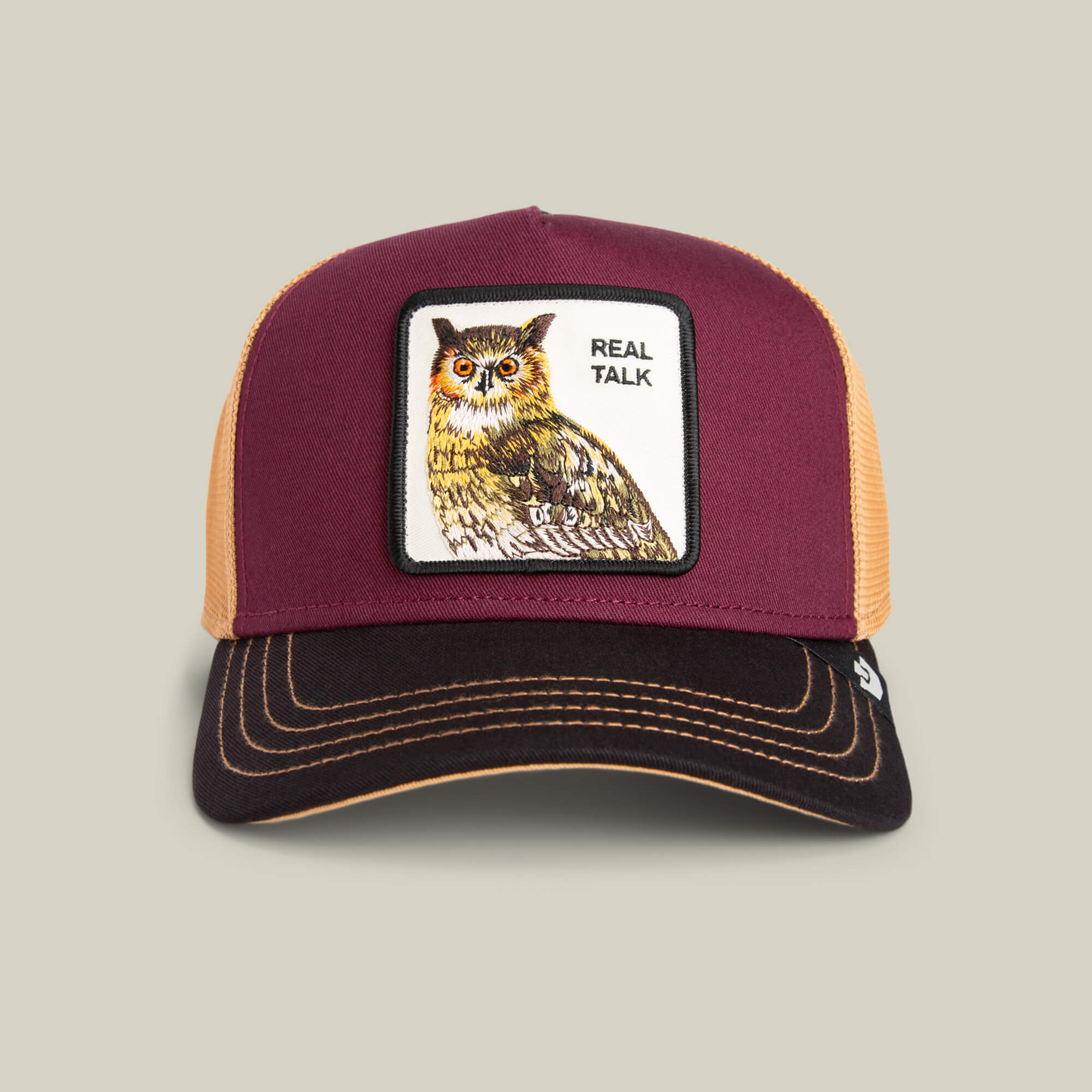The Goorin Bros. Tricolor Owl trucker hat features a maroon owl patch with "REAL TALK" text on the front, tan mesh, and a black brim.