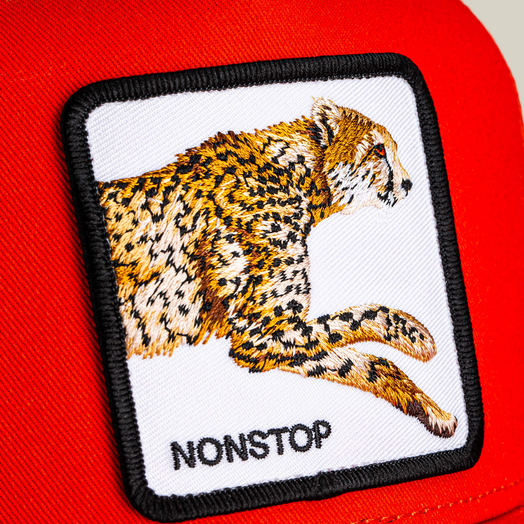 Close-up of "The Nonstop Cheetah" patch by Goorin Bros., featuring a running cheetah and the word NONSTOP on vibrant red fabric, capturing the cat's speed.