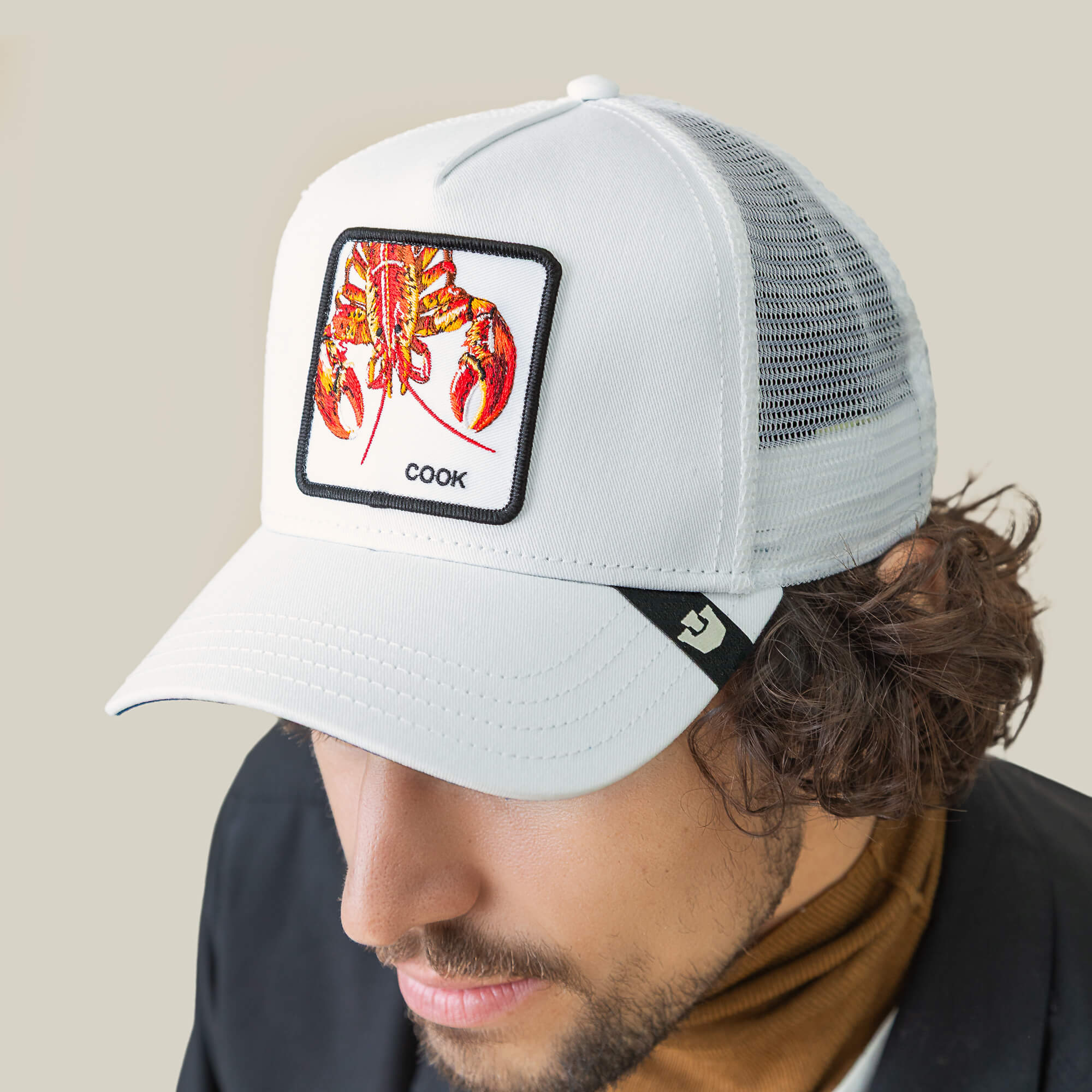 Someone wears the Goorin Bros. Lemme Cook white mesh back trucker hat, featuring a playful illustrated lobster patch and the word "COOK" on front.