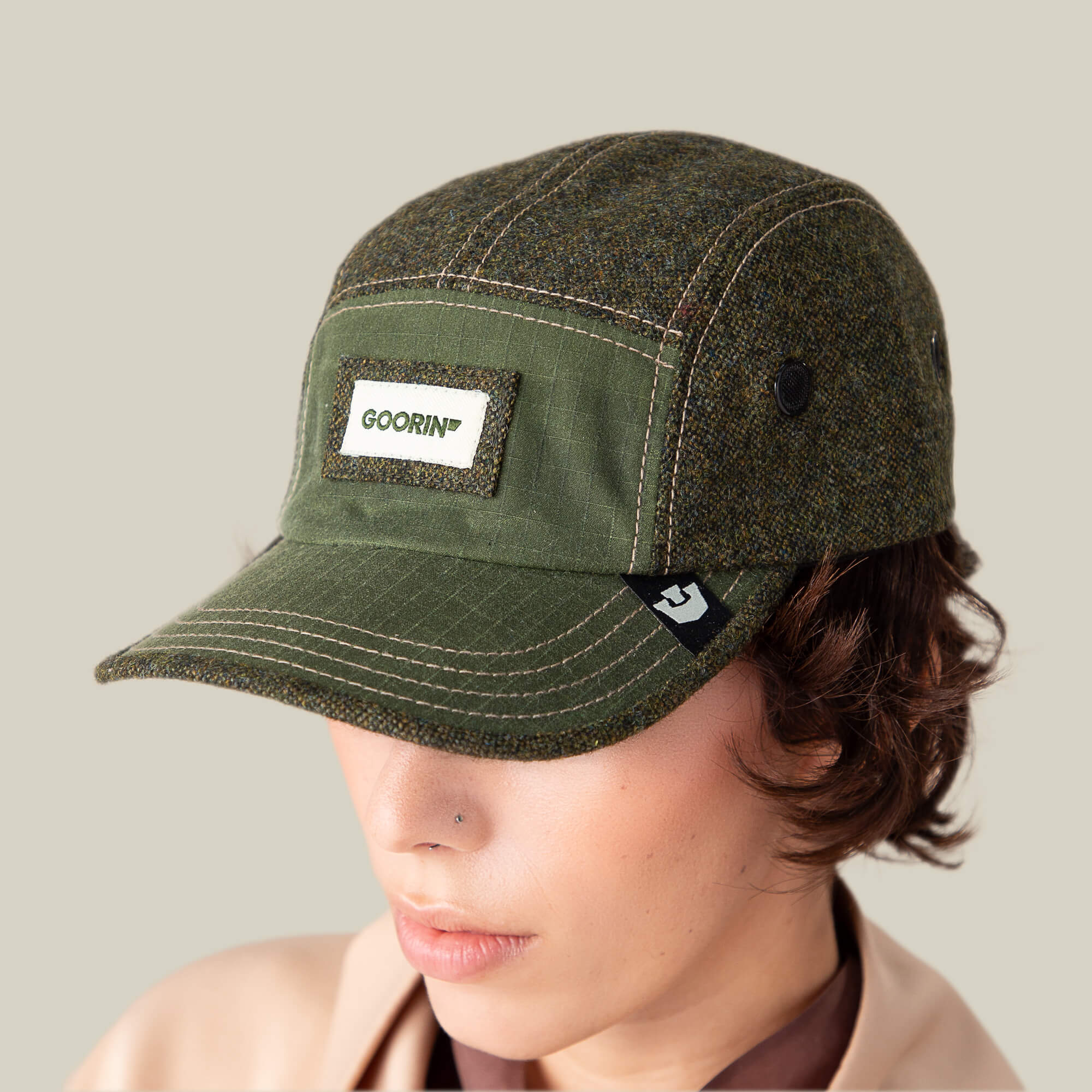 A person wearing a Goorin Bros. Billed Demand field hat in olive green with a curved brim and a visible Goorin Bros. patch on the front, set against a neutral background.