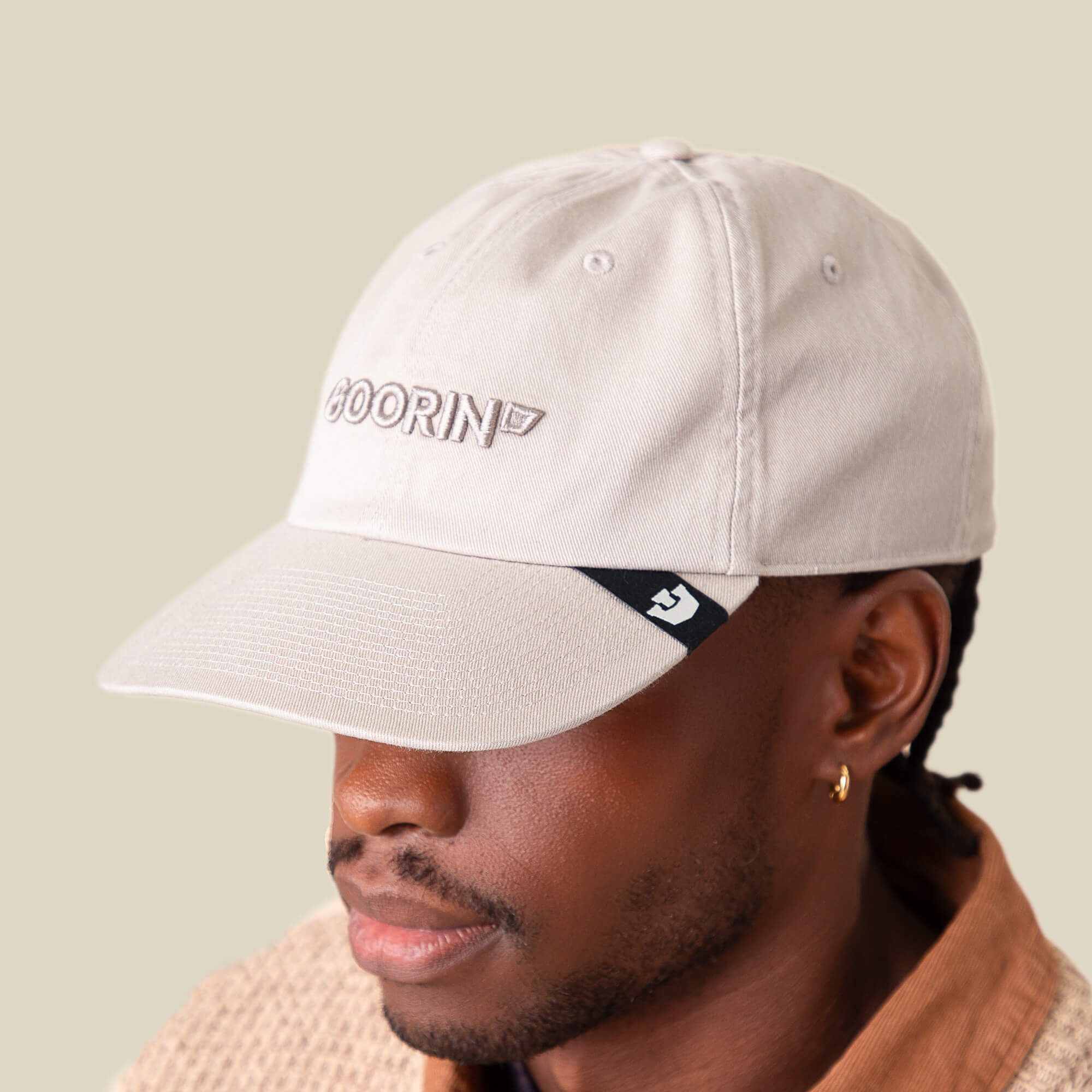 A person wears the Goorin Bros. Papa Core light beige baseball hat, featuring a soft crown, "GOORIN" embroidered on the front, and a small black tag on the curved brim, facing slightly downward.