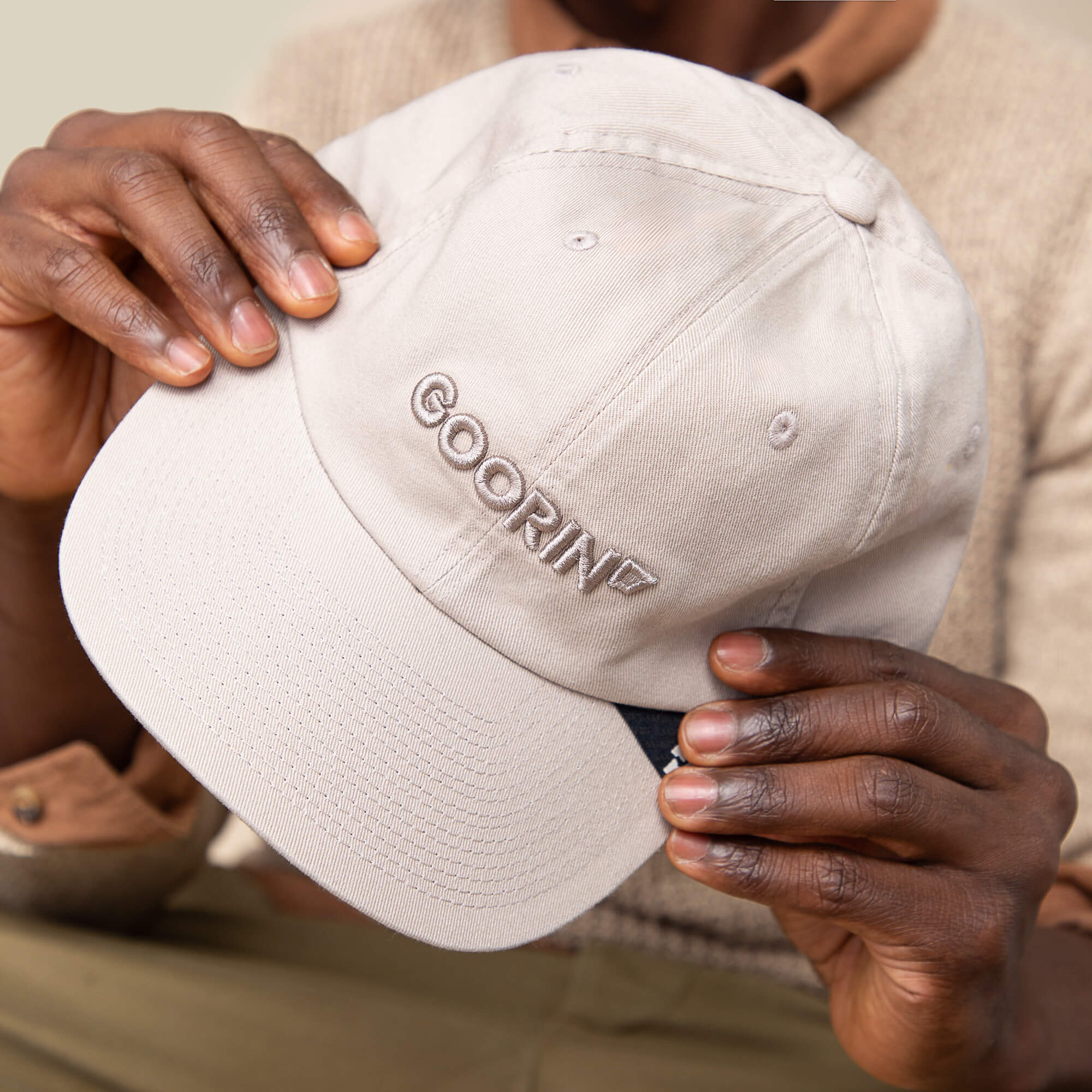 A person holds the Papa Core hat by Goorin Bros., featuring a beige color, soft crown, and GOORIN embroidered on the front.