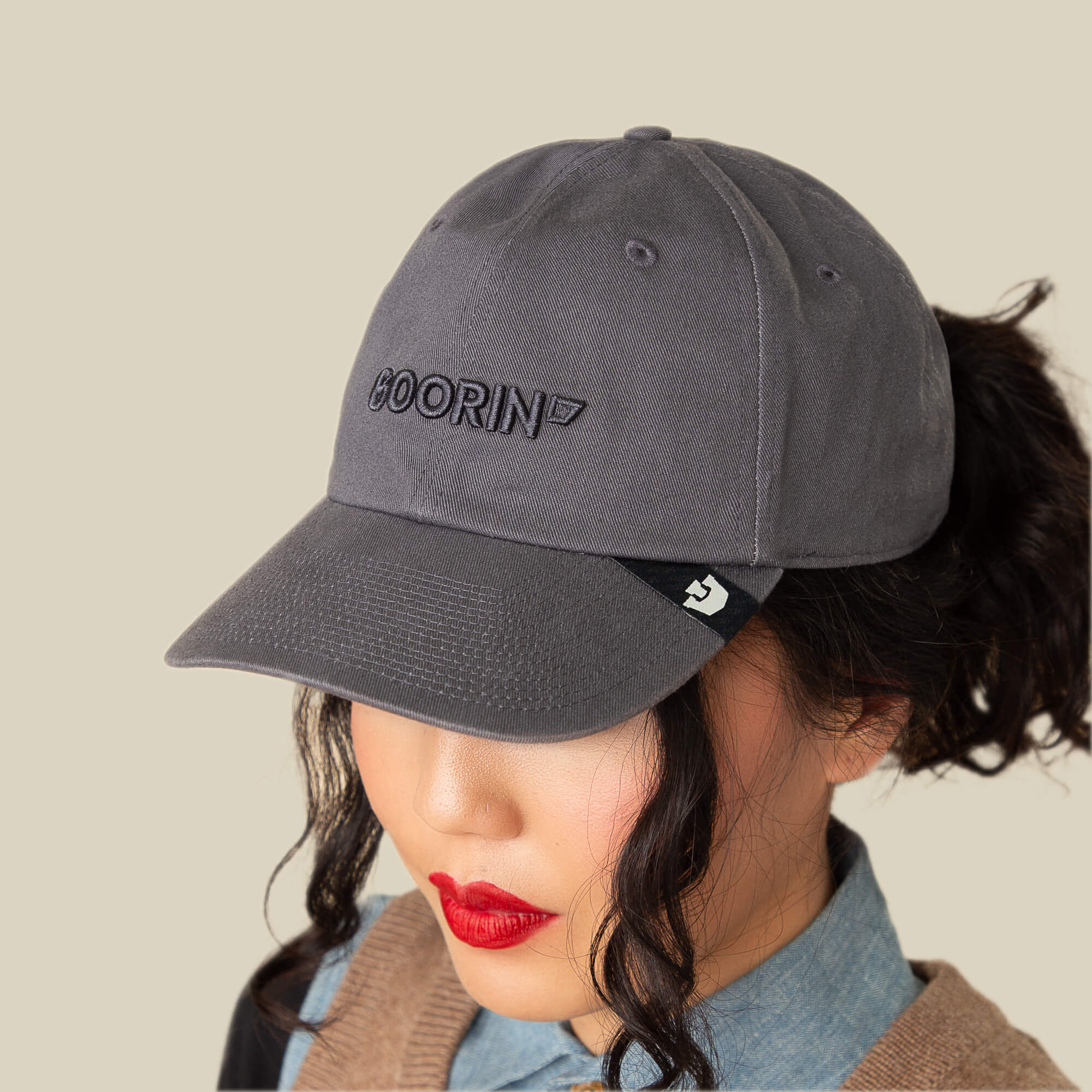 Wearing the Papa Core hat by Goorin Bros. with a soft crown and curved brim, a person with red lipstick and curled hair pairs it with a denim shirt and tan sweater, facing slightly downward.