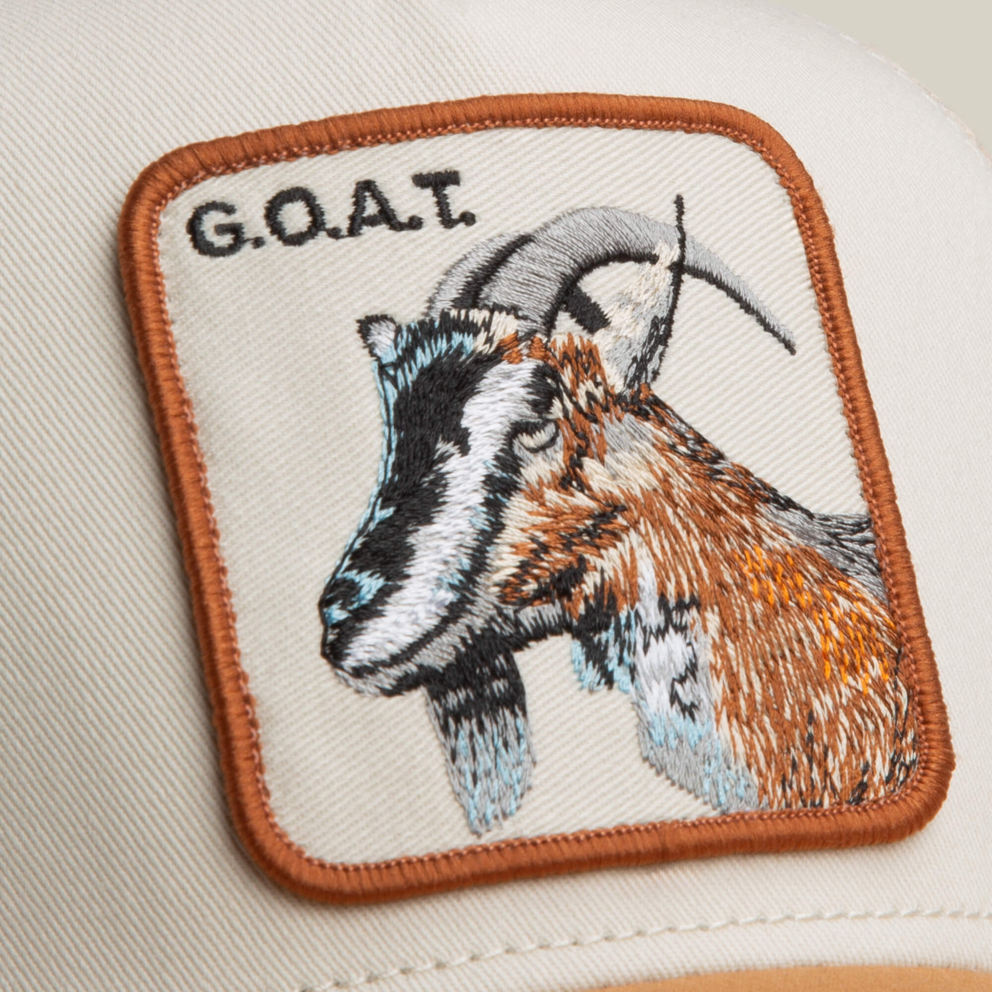 Close-up of The G.O.A.T by Goorin Bros.—a beige hat in neutral tones, featuring a bold patch with an embroidered goat’s head and the text "G.O.A.T.