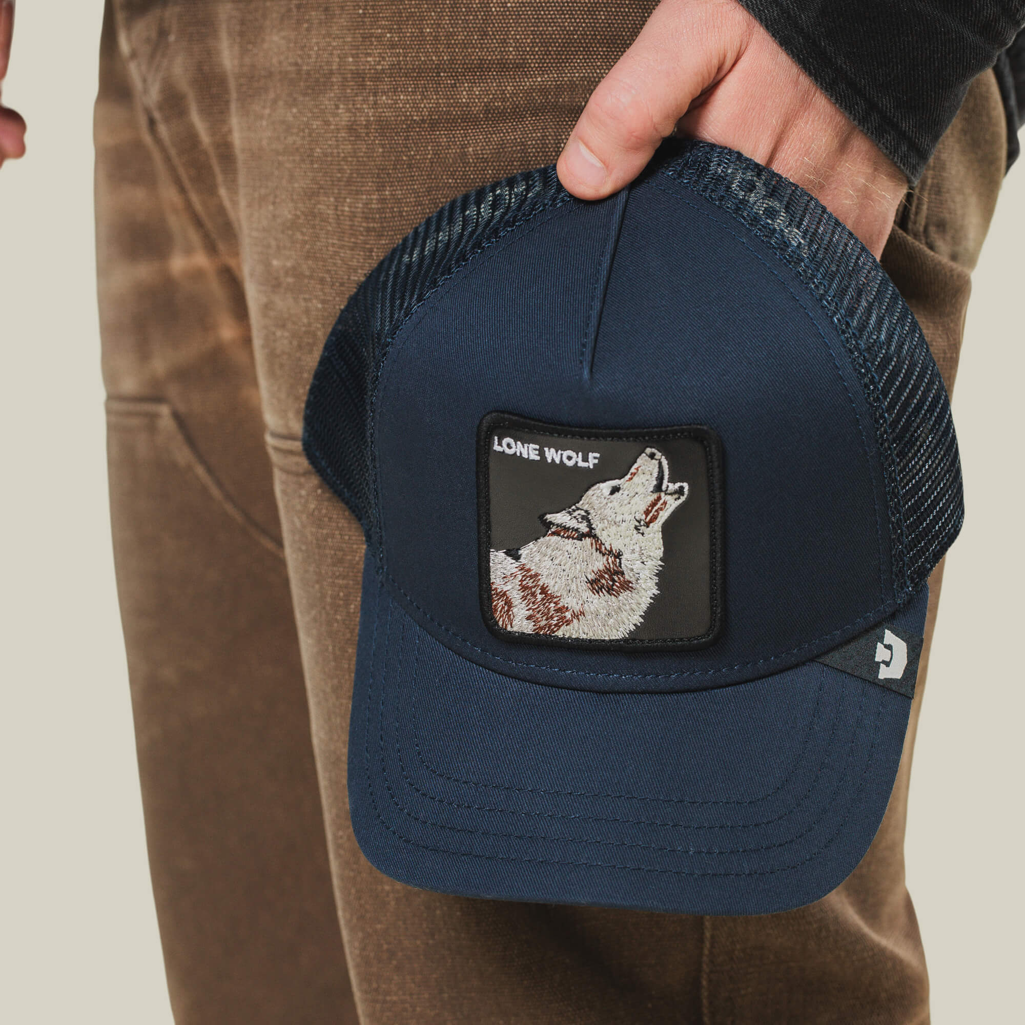 A person holds The Lone Wolf, a navy blue trucker hat by Goorin Bros., featuring a howling wolf patch and "LONE WOLF" embroidery for true outlaw style.
