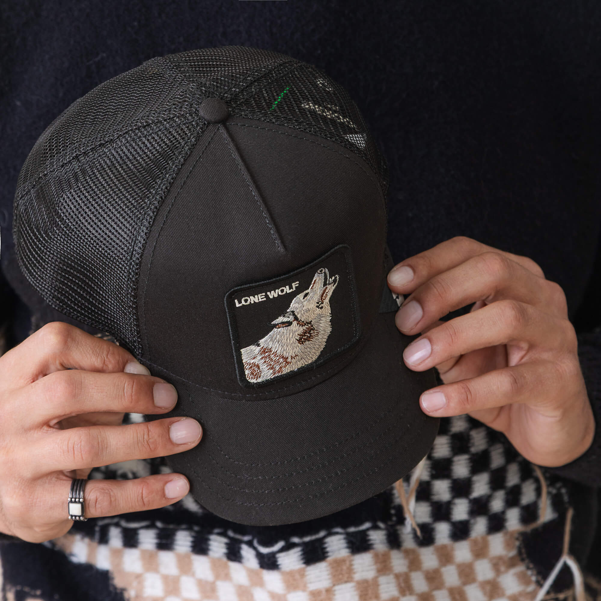 A person holds The Lone Wolf trucker hat by Goorin Bros., featuring a black mesh design and a patch with a howling wolf and "LONE WOLF," capturing true outlaw energy.