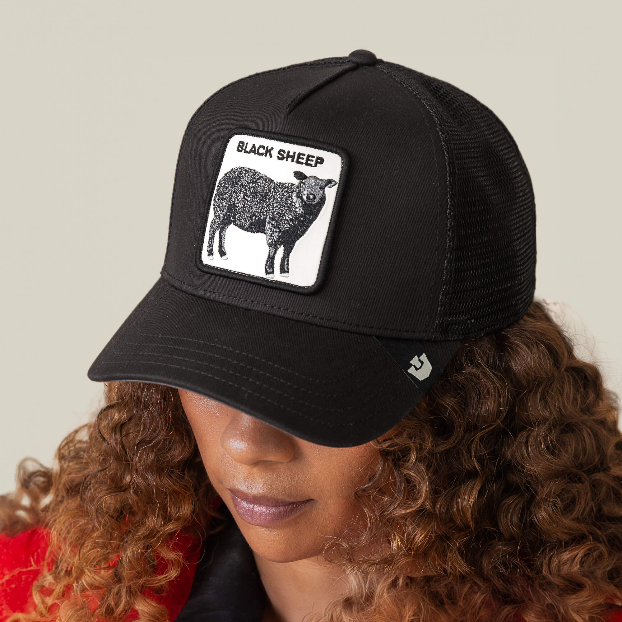 A person with curly hair wears Goorin Bros.' "The Black Sheep" black baseball cap, featuring a patch with a black sheep illustration and the words BLACK SHEEP—perfect for those who love to stand out.