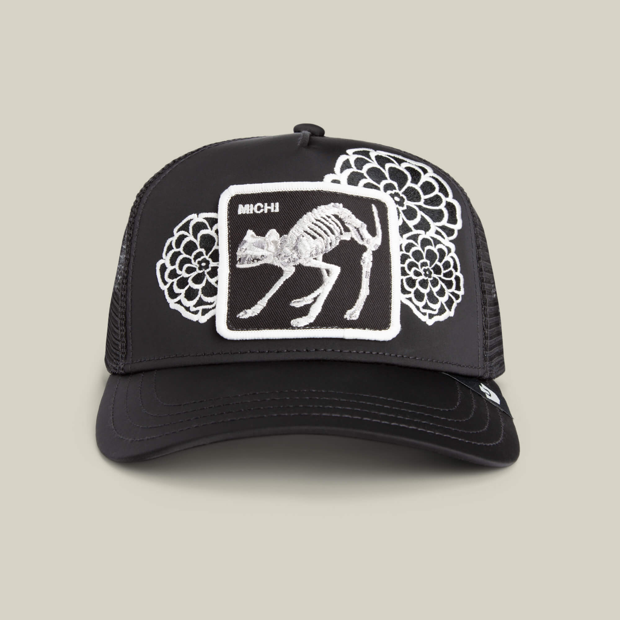 The Dia De Michi VOID trucker hat by Goorin Bros. features a crown patch with an embroidered animal skeleton, oversized florals in white thread, and "MICHI" above the skeleton.