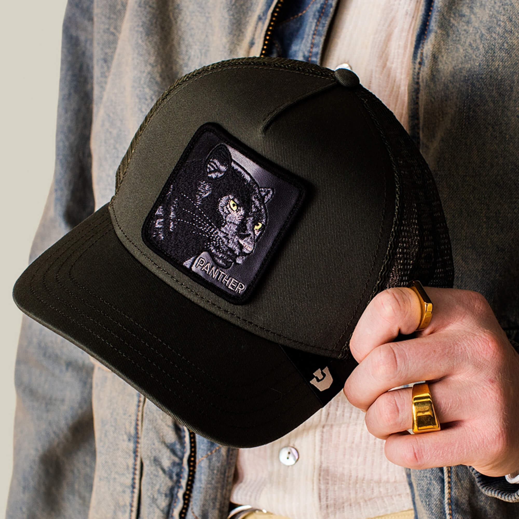 A person holding The Panther by Goorin Bros., a sleek black trucker hat with a patch featuring an embroidered panther and the word "PANTHER.
