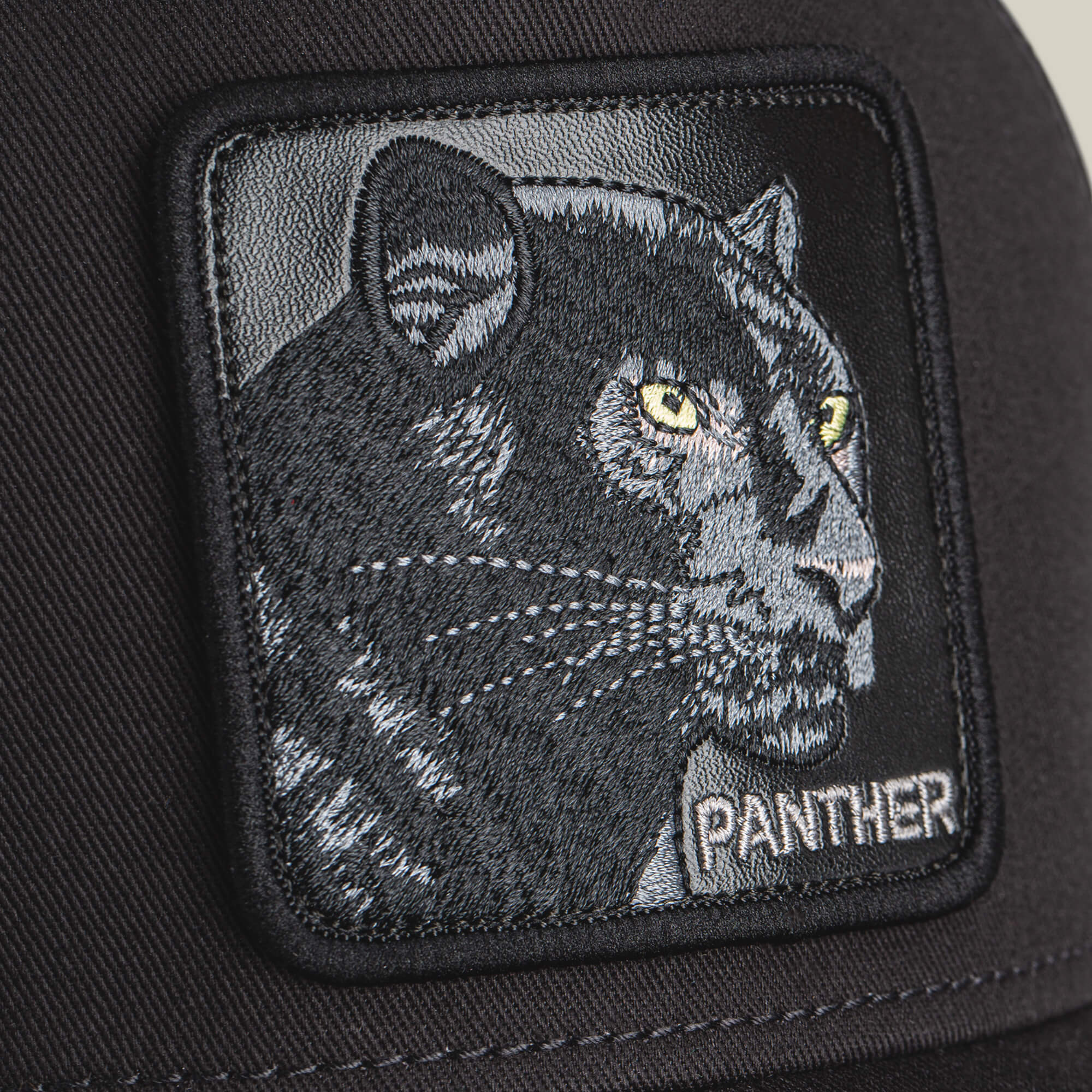 A close-up of The Panther by Goorin Bros., a black fabric patch with an embroidered panther featuring yellow eyes and "PANTHER" in white—ideal for adding bold style to any panther or black hat.