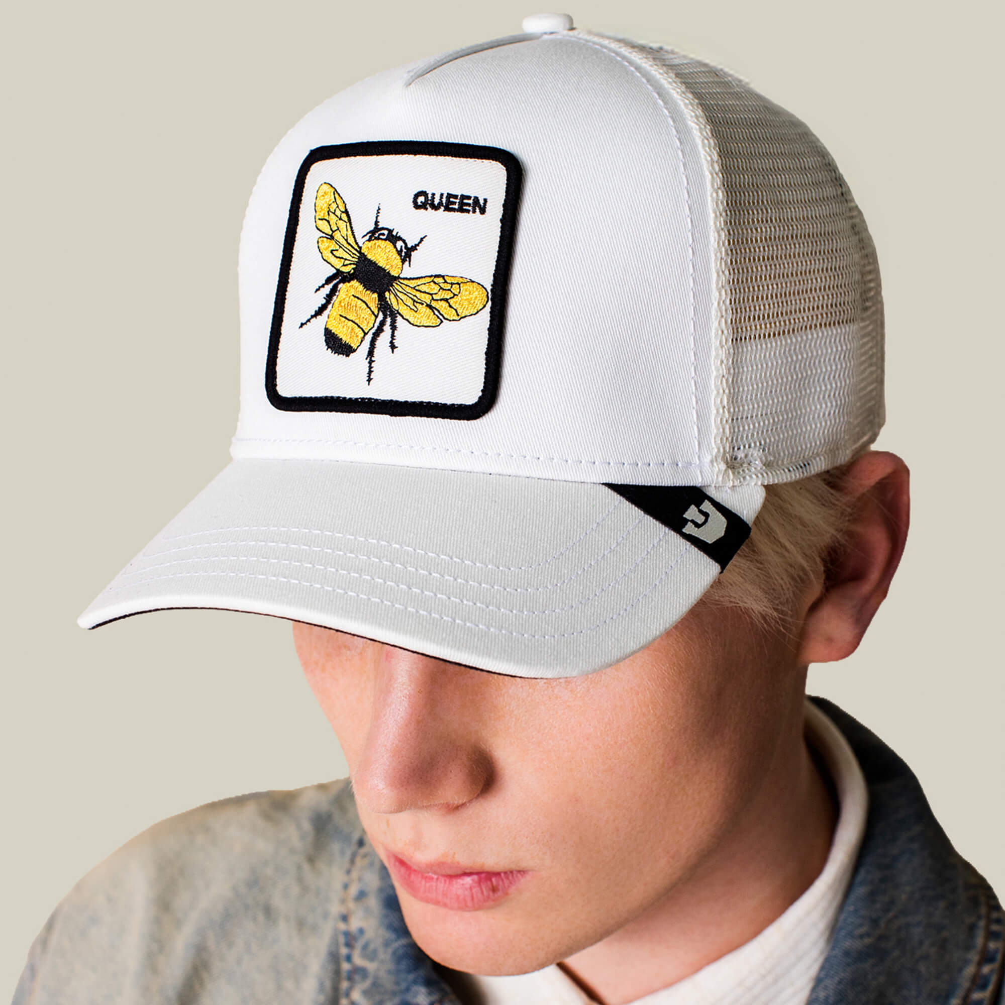 A person wearing the Goorin Bros. Queen Trucker hat, which features a yellow bee and the word QUEEN on its patch, looks downward.