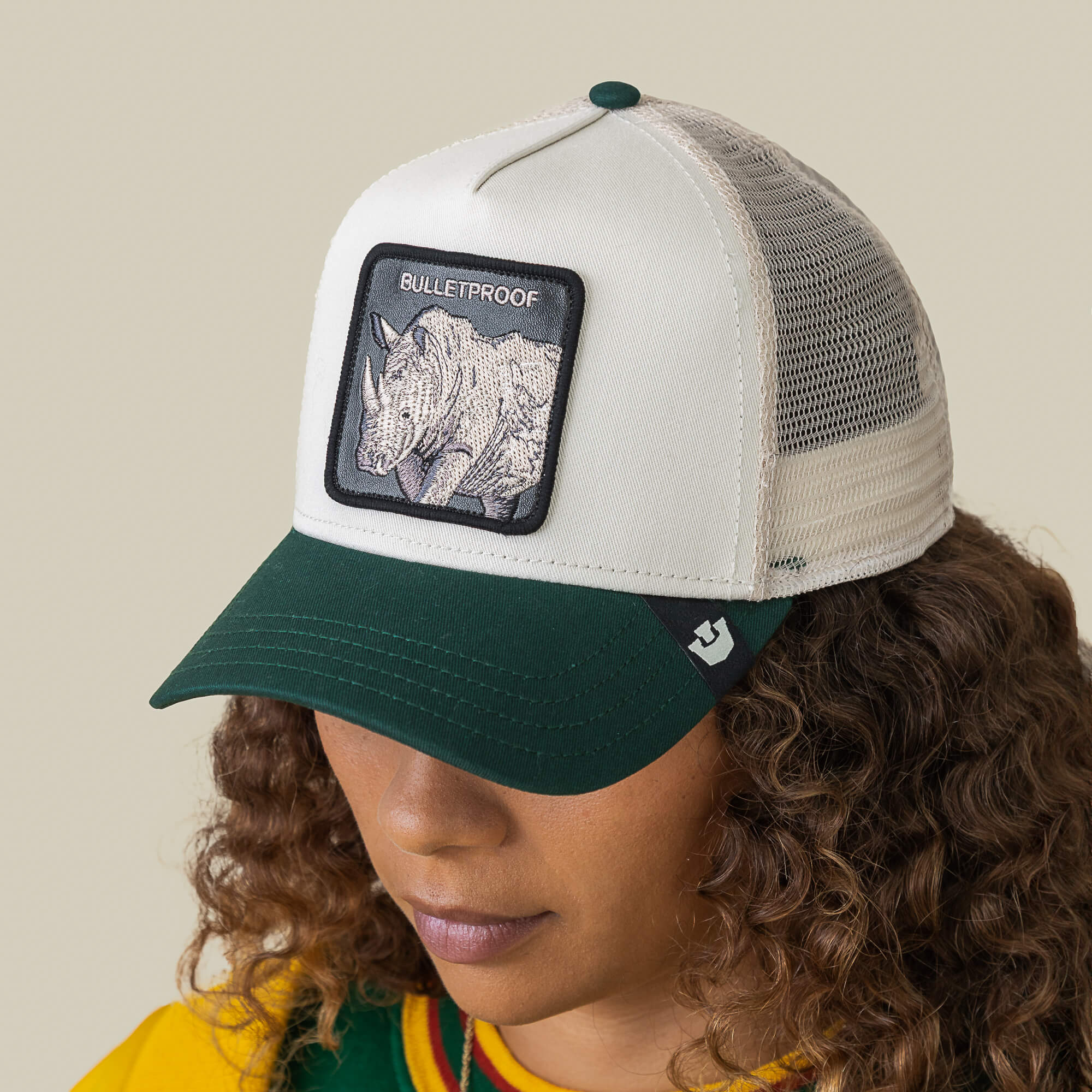 Someone sports the Goorin Bros. Bulletproof Trucker, a hat with a rhino patch labeled BULLETPROOF, white front, green bill, and mesh back—designed for tough looks inspired by rhino armor and bold street style.