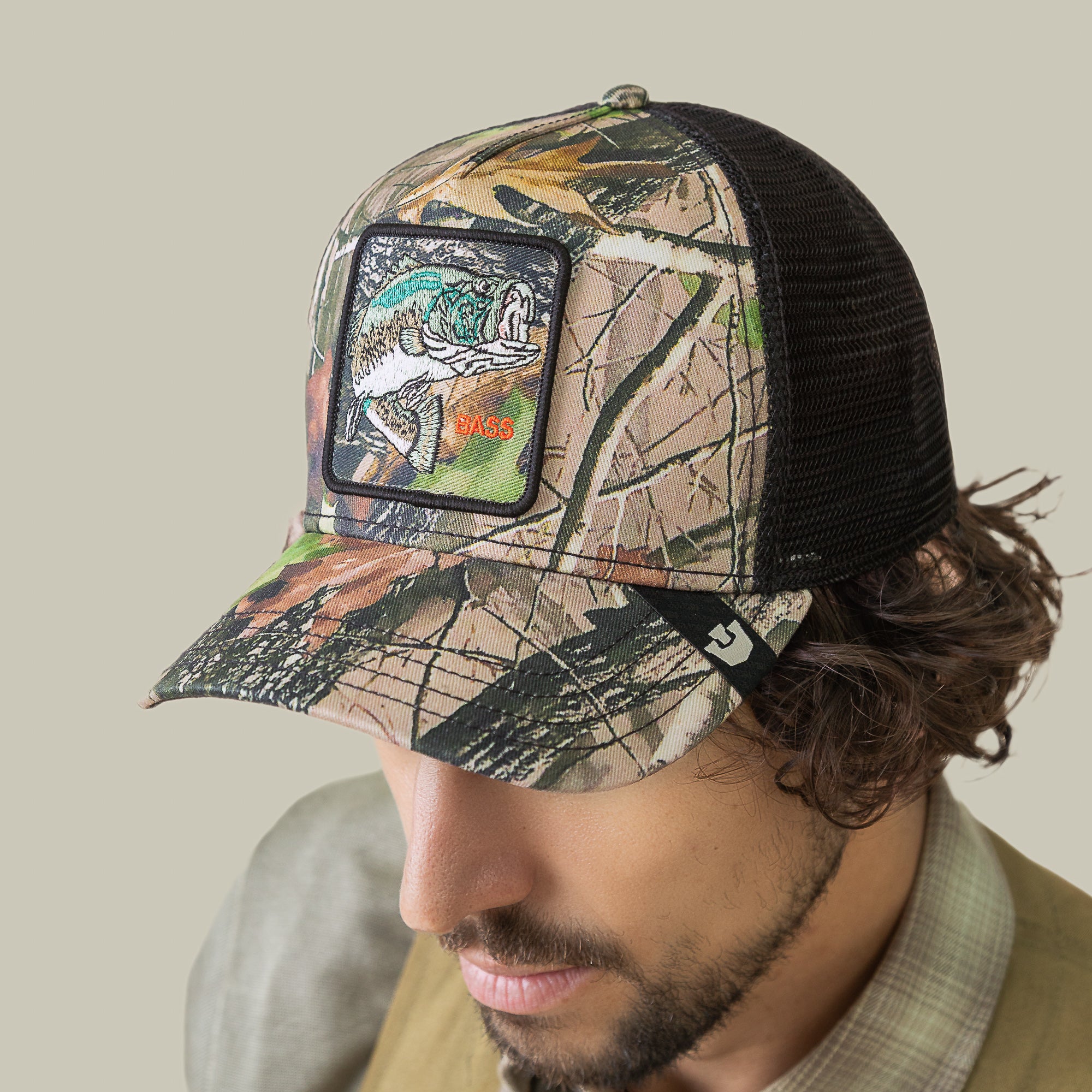 A man wearing the Goorin Bros. Camouflage Bass mesh trucker hat featuring a hyperrealistic embroidered bass patch on the front.