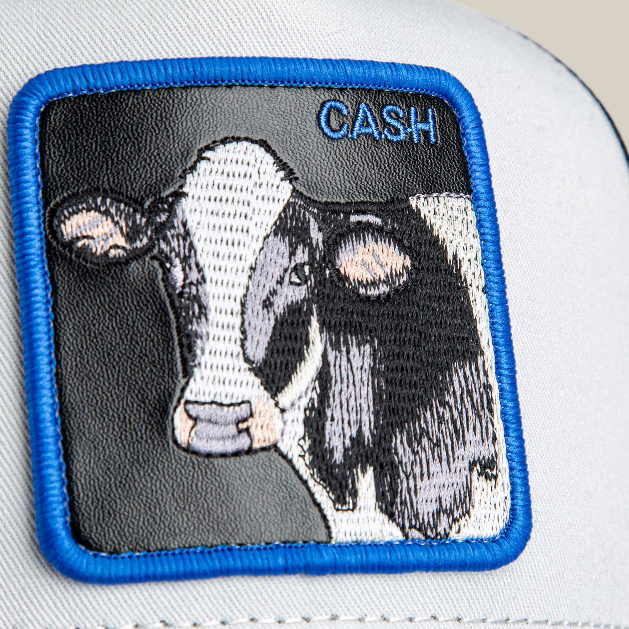 Close-up of the Goorin Bros. "Tricolor Cow" patch, embroidered on white fabric with a blue border—a unique accessory for wallet or cow lovers.