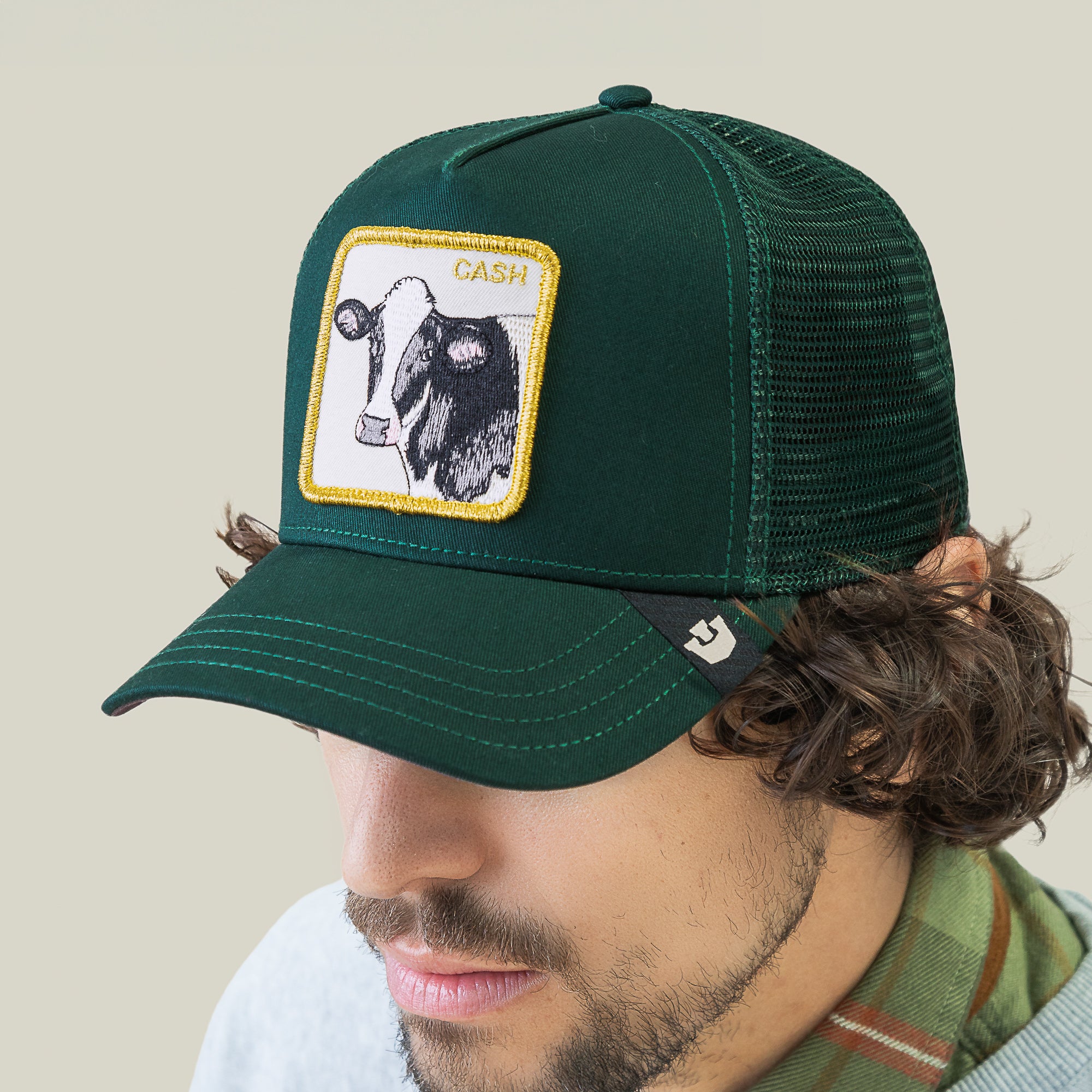 A man wears the Goorin Bros. Cash Cow Trucker cap, featuring a green design with a bold bovine patch and "Cash Cow" embroidered above the cow image.