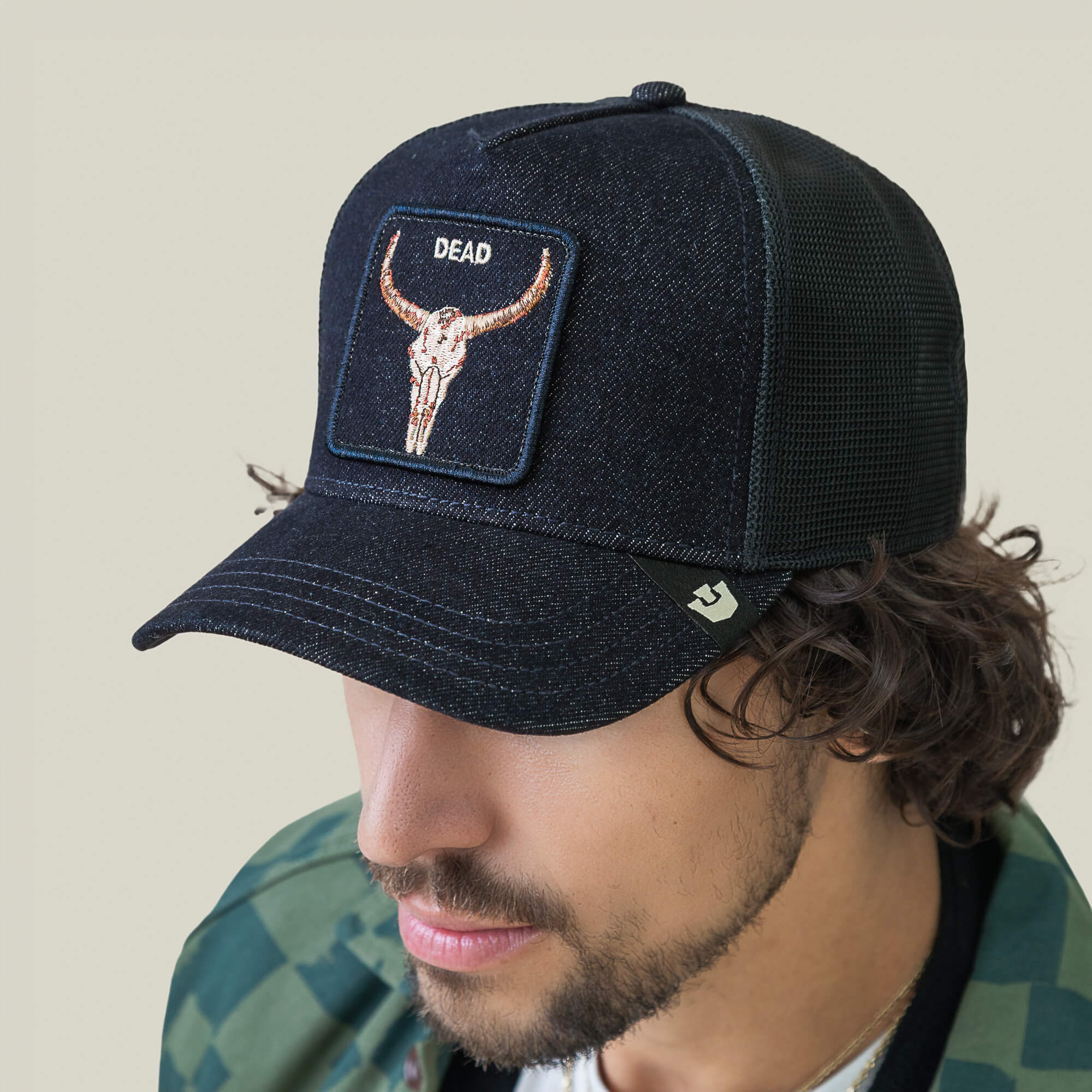 A man in a Goorin Bros. Denim Dead black mesh biker cap with bull skull embroidery and a green camo jacket, seen from an angled, overhead view.