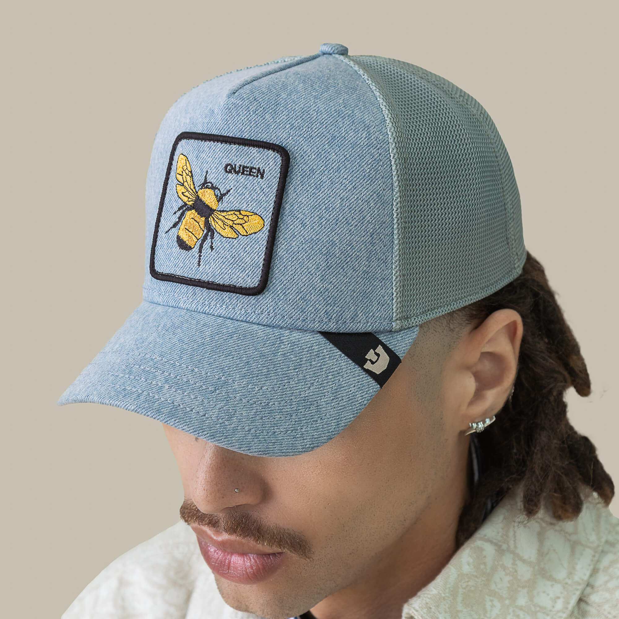 A person wearing a Goorin Bros. Denim Queen trucker mesh cap with a patch of a yellow bee and the word QUEEN on the front, topped with embroidered royalty, seen from a slightly elevated angle.